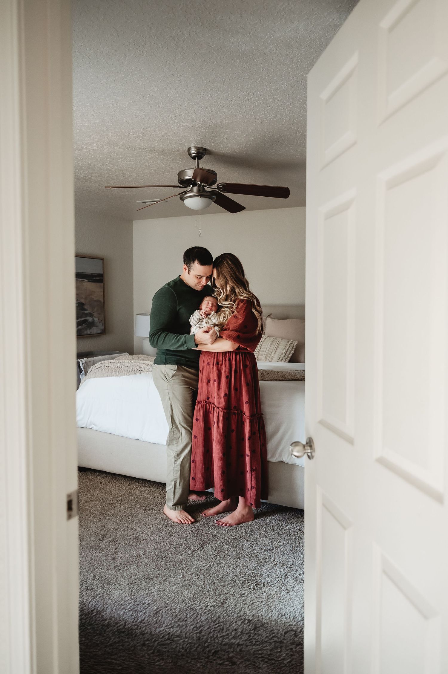 Couple shares intimate moment sitting on gray carpet in bright minimalist bedroom with white walls and ceiling fan.