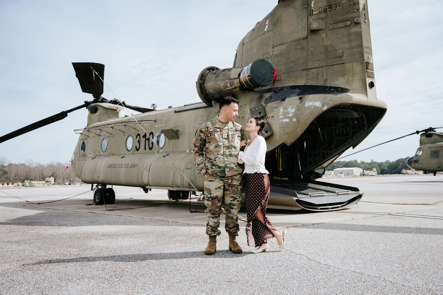 Military personnel stand near a CH-47 Chinook helicopter on an airfield during a maintenance operation.