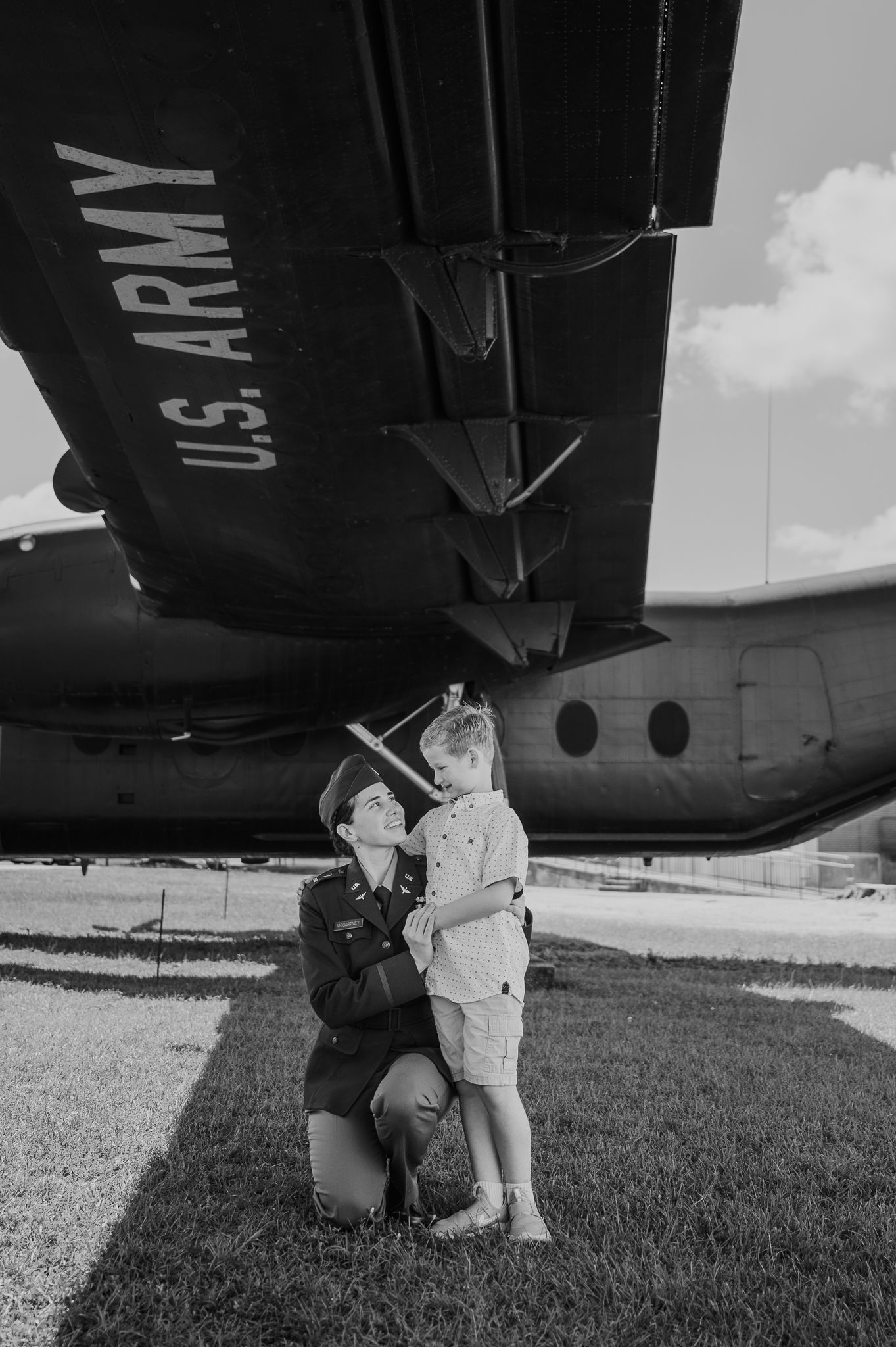 U.S. Army soldier kneeling with young child under military aircraft in black and white photo.