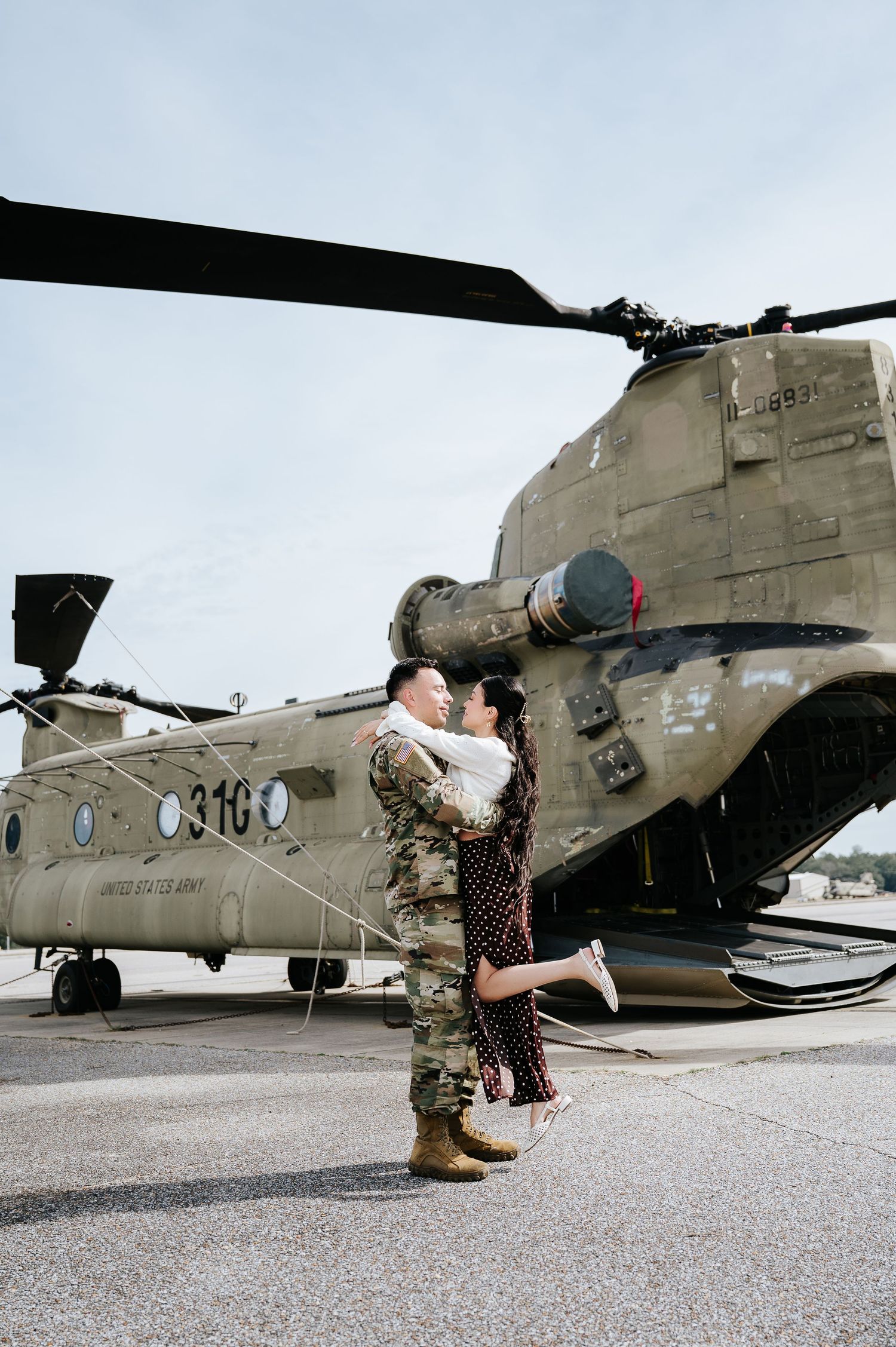 Military helicopter engagement photo session showing couple posing near a CH-47 Chinook aircraft on tarmac.