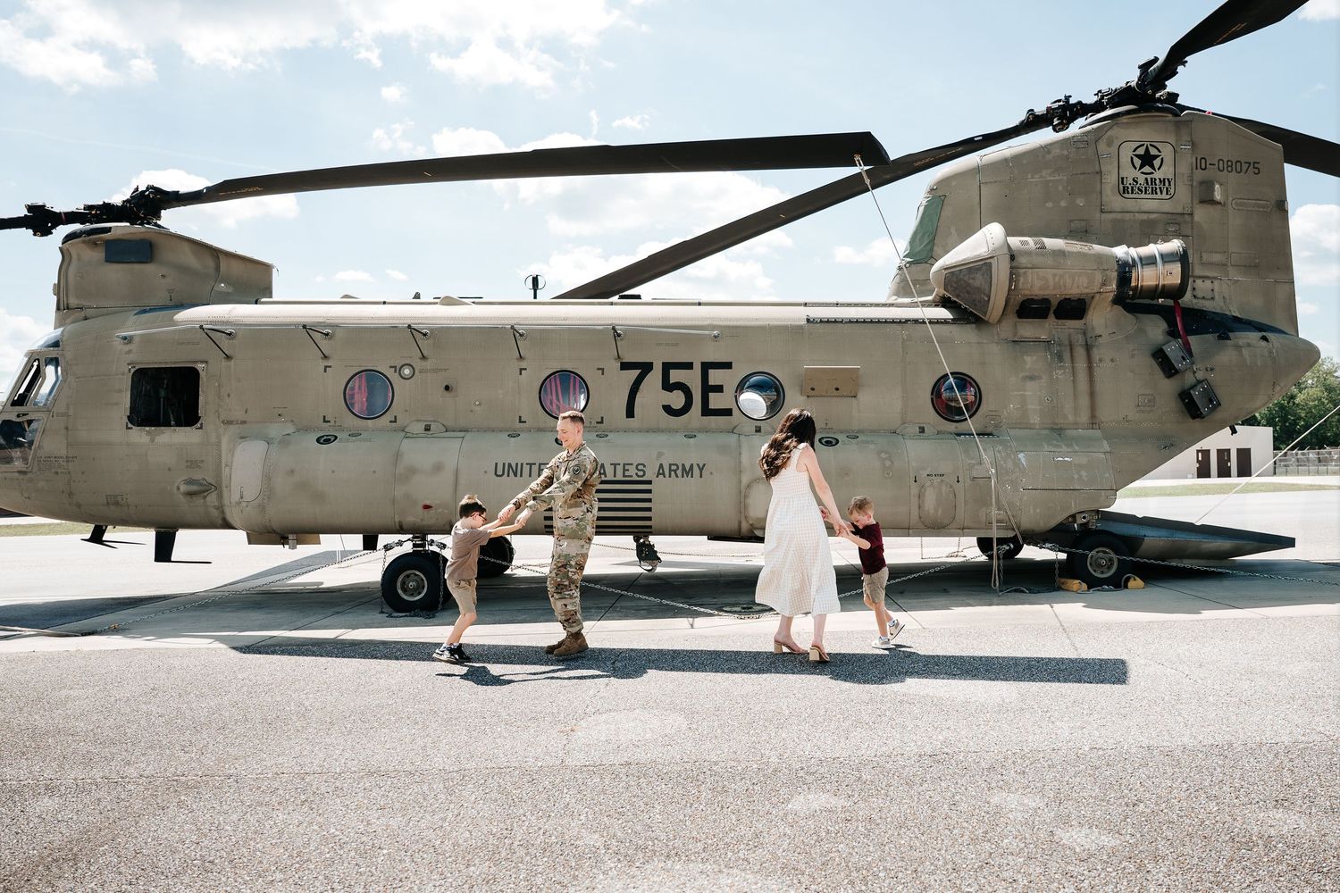 Family walking near a U.S. Army CH-47 Chinook helicopter numbered 75E outdoors.