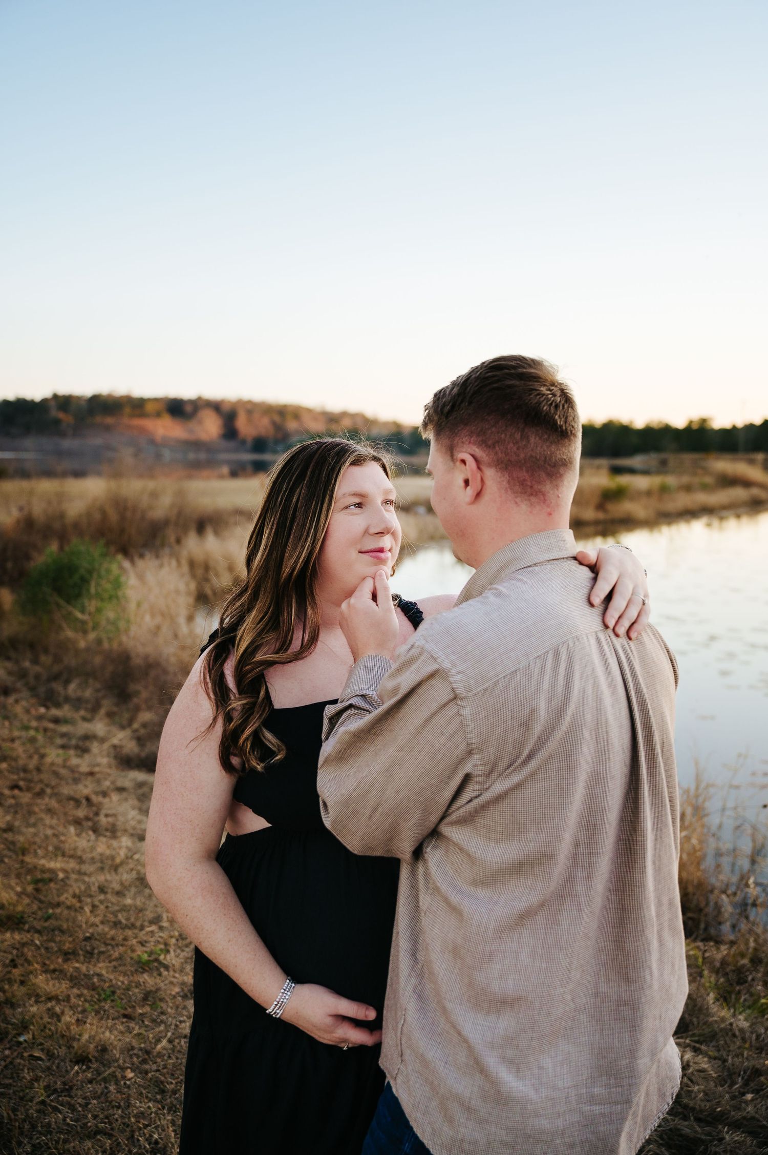A couple shares an intimate moment together by a lake during sunset in a natural outdoor setting.