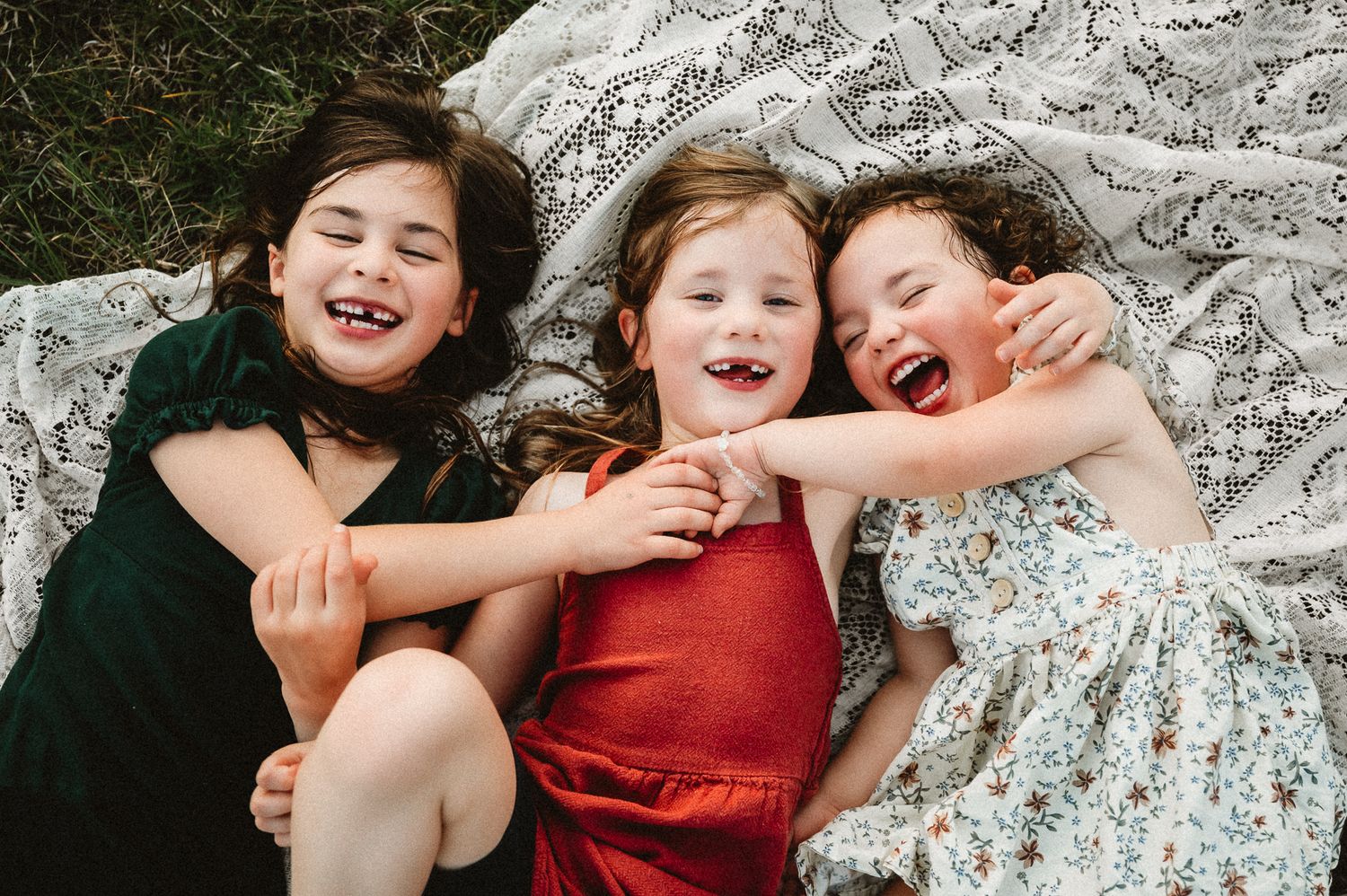 Three children laying on a white blanket laughing and playing together outdoors.