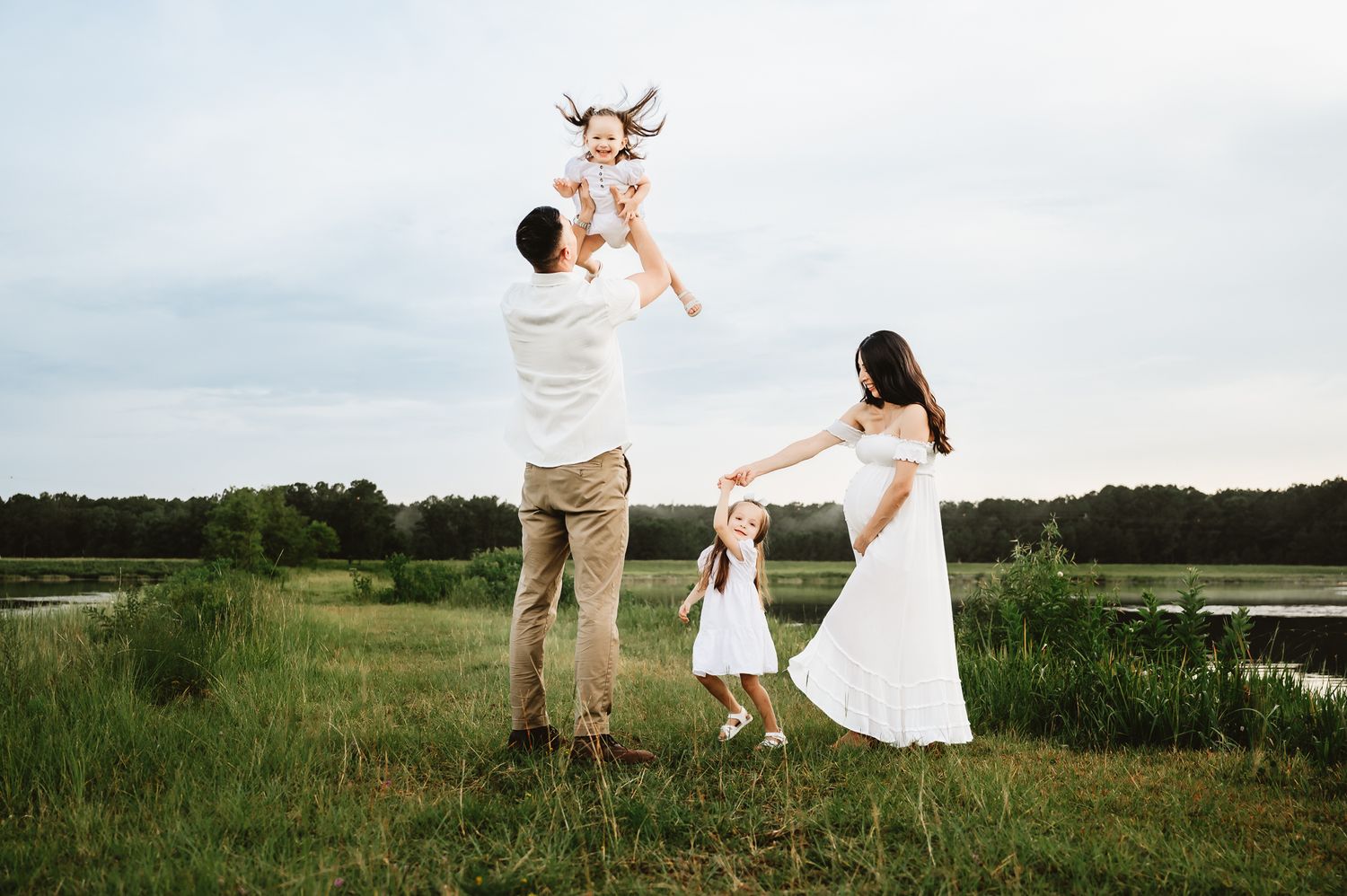 Family enjoying playful moments together in a scenic meadow by a lake during golden hour.