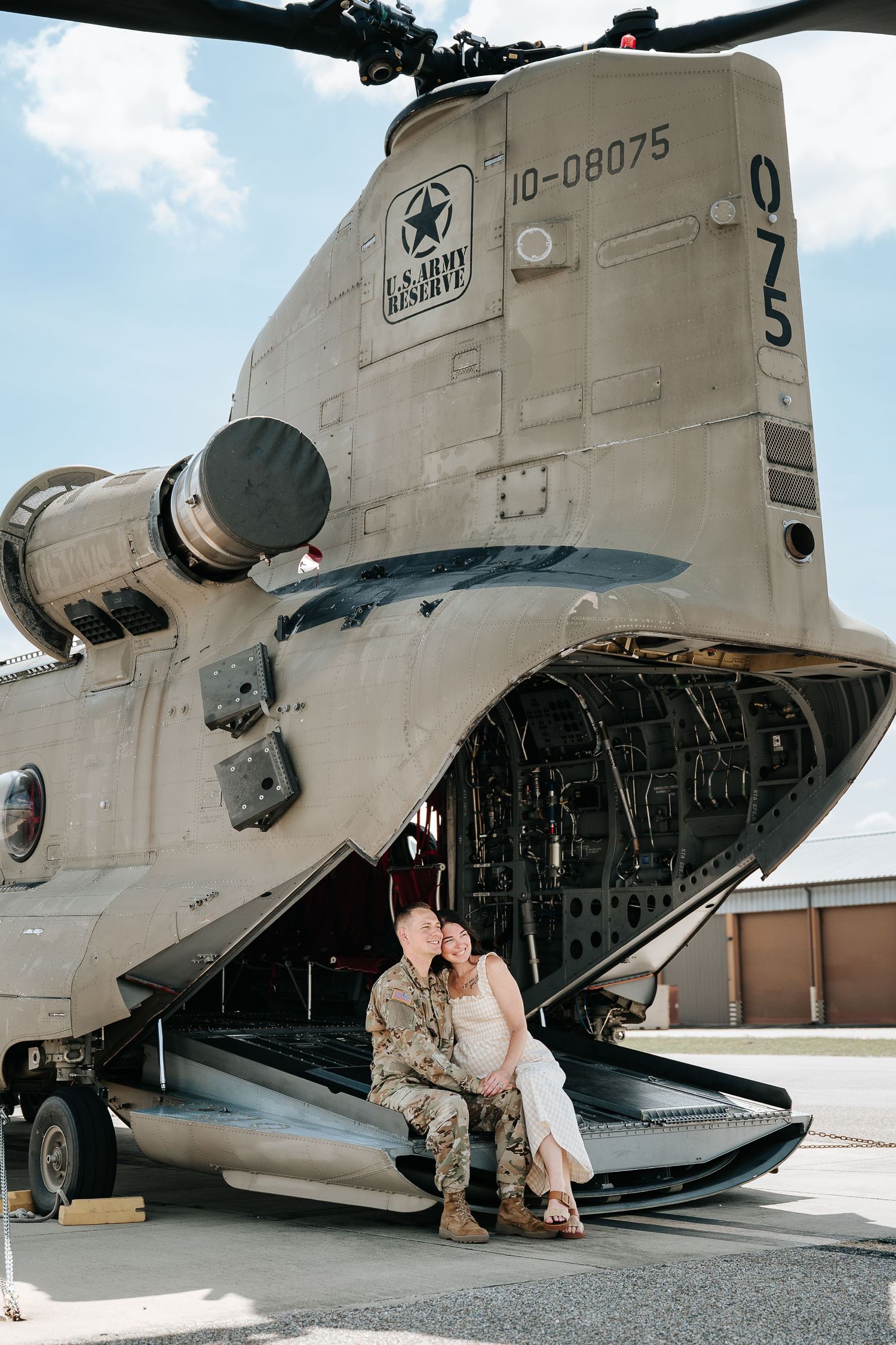 Couple sharing a romantic kiss in front of a U.S. Army Reserve CH-47 Chinook helicopter on a military base.