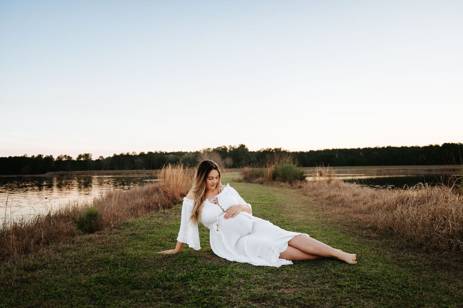 A couple in wedding attire poses together in a rustic field at sunset creating romantic silhouettes against the sky.