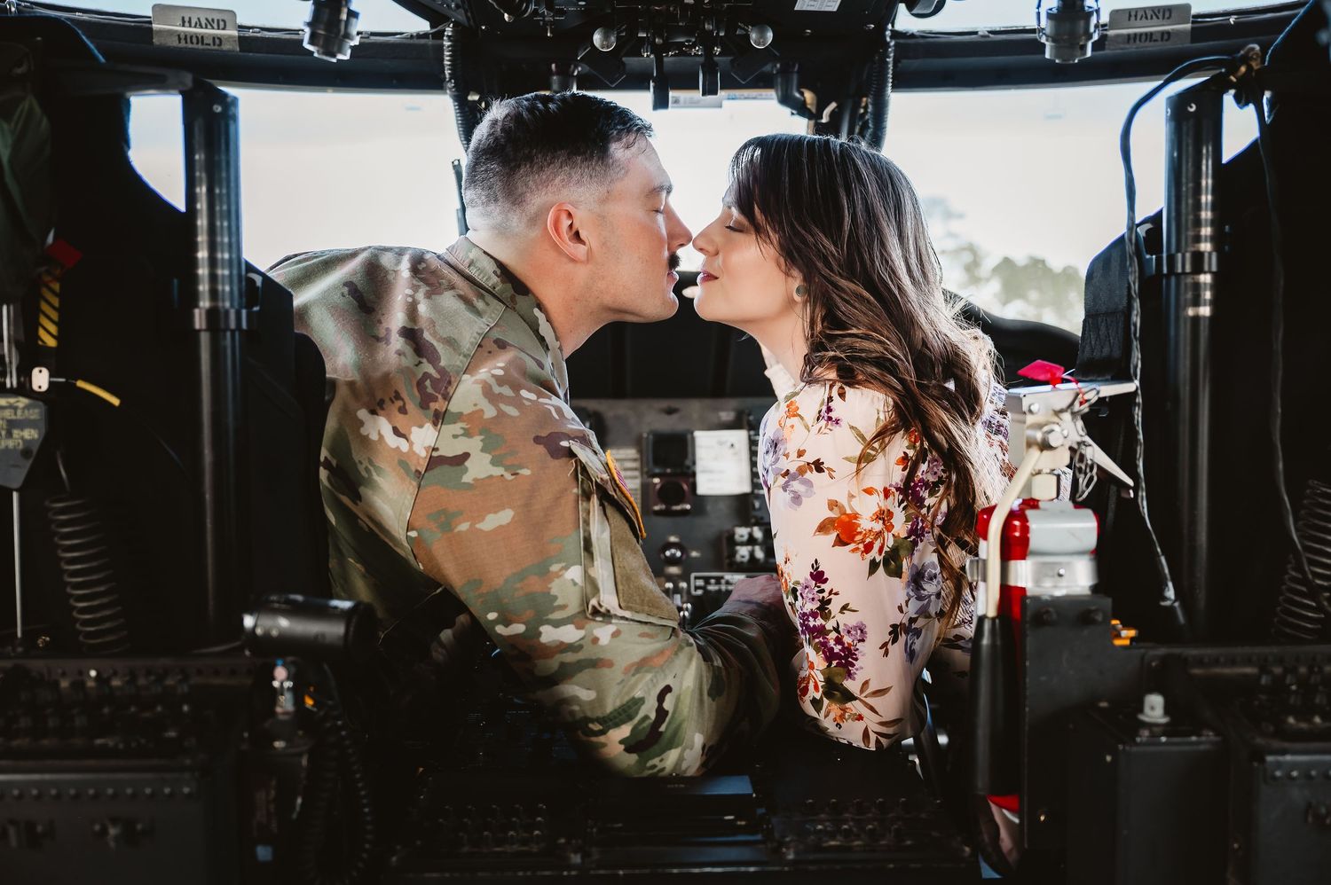 A romantic couple shares an intimate kiss in front of a military helicopter during a wedding photo session.