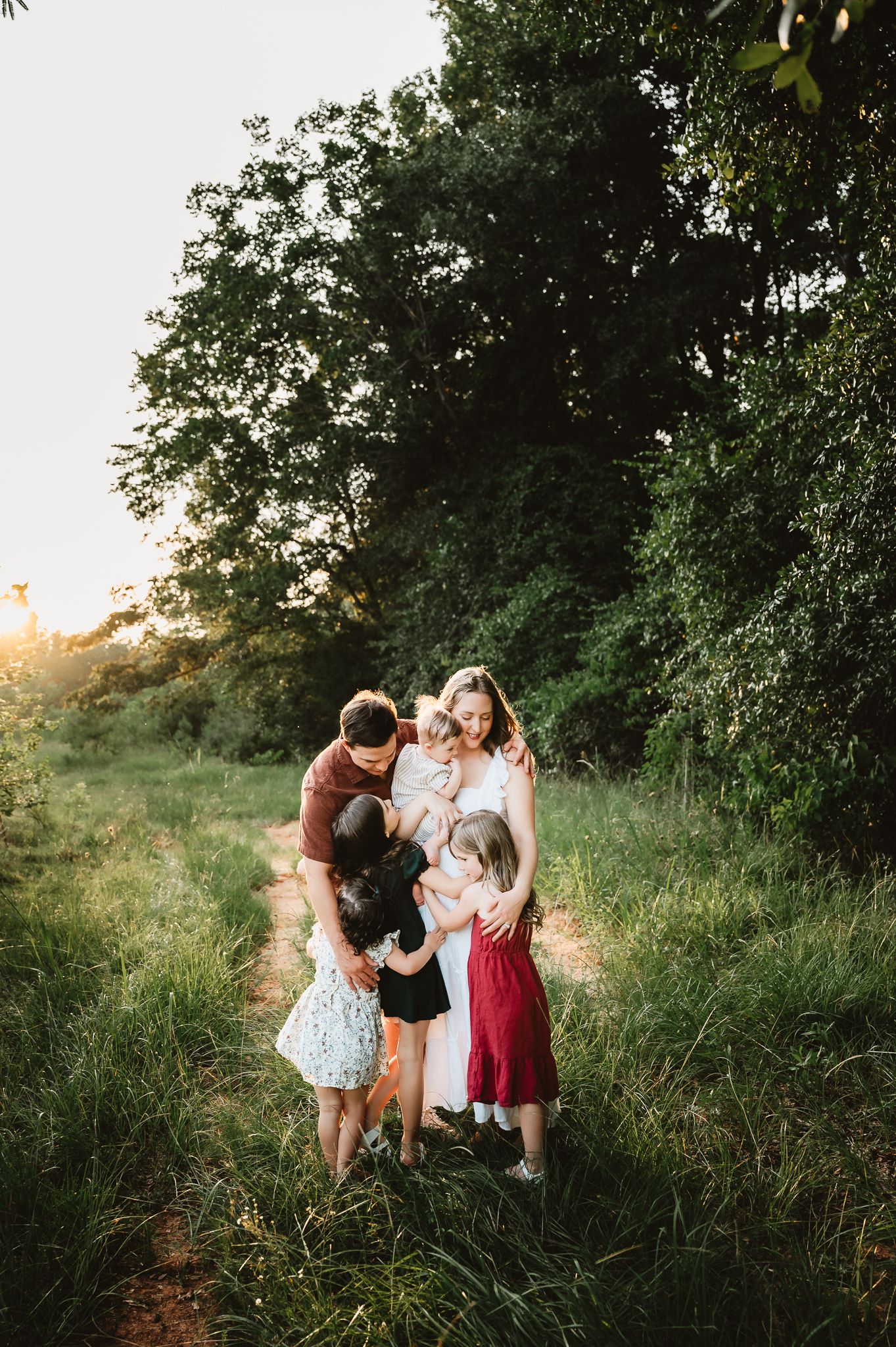 A group shares a tender moment together on a sunlit nature path surrounded by lush greenery at golden hour.