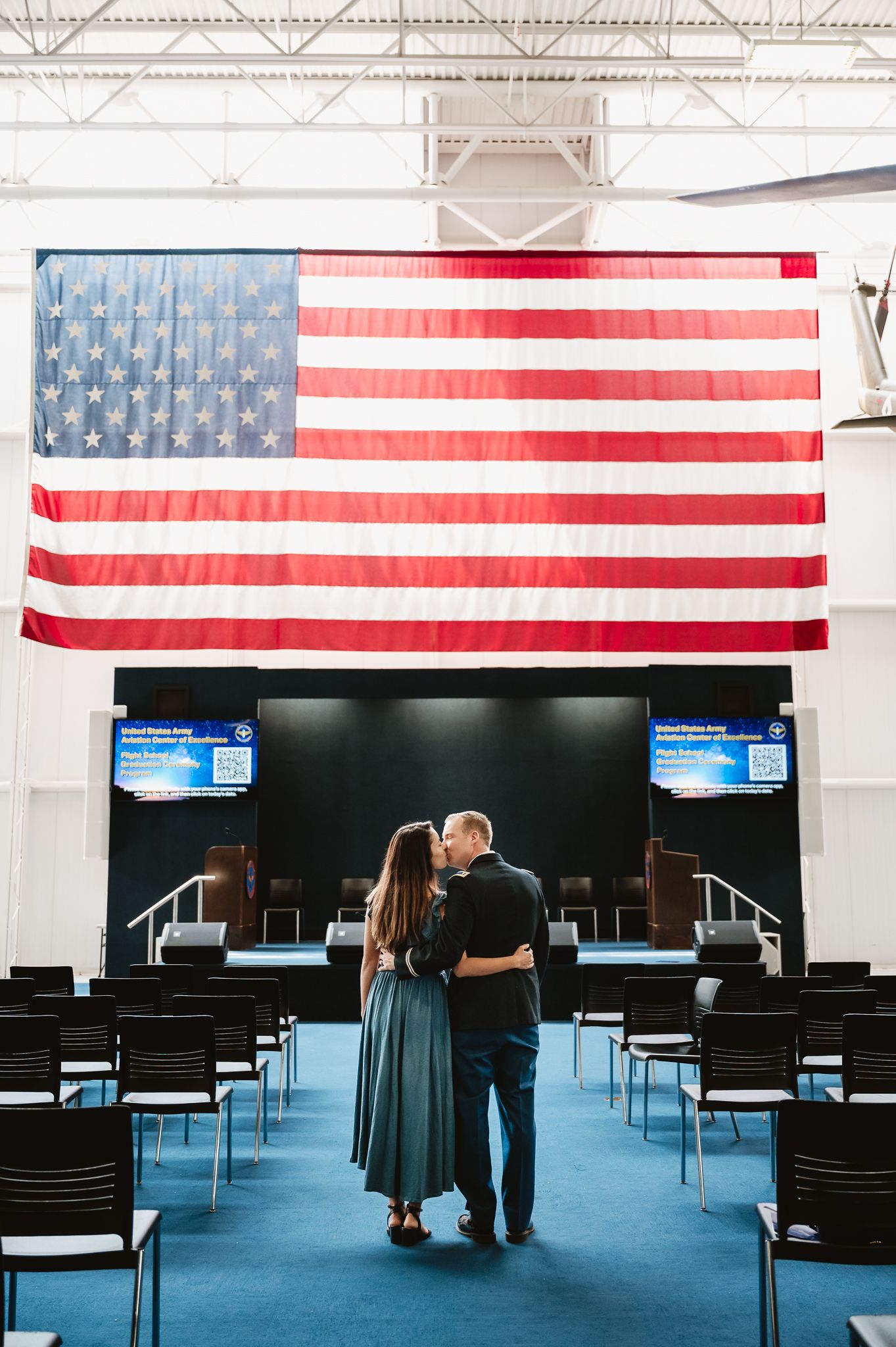 Couple walking across a blue carpeted room with American flags hanging on the wall.