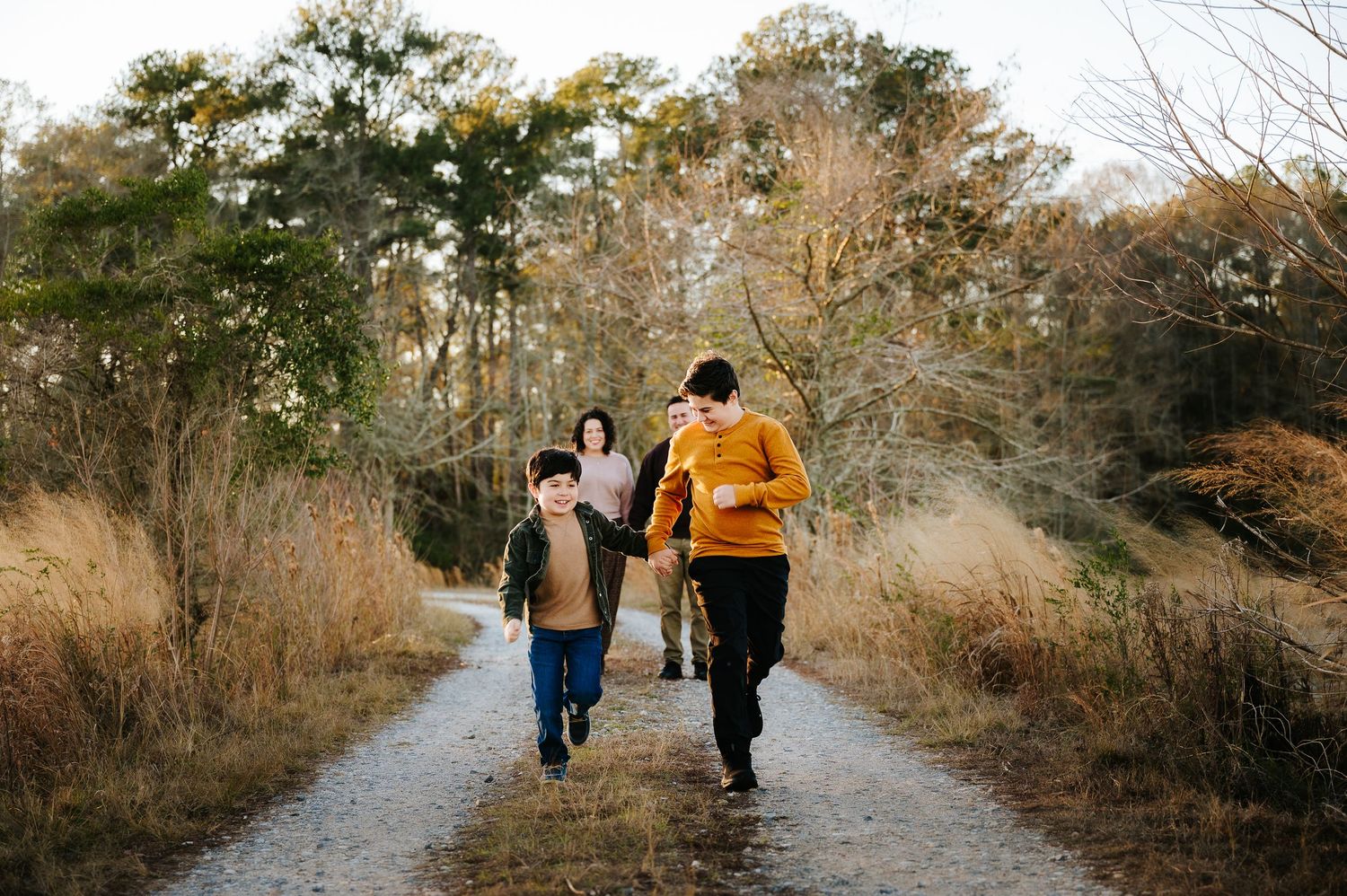 People walking together on a scenic autumn trail through dried grass and bare trees on a sunny day.