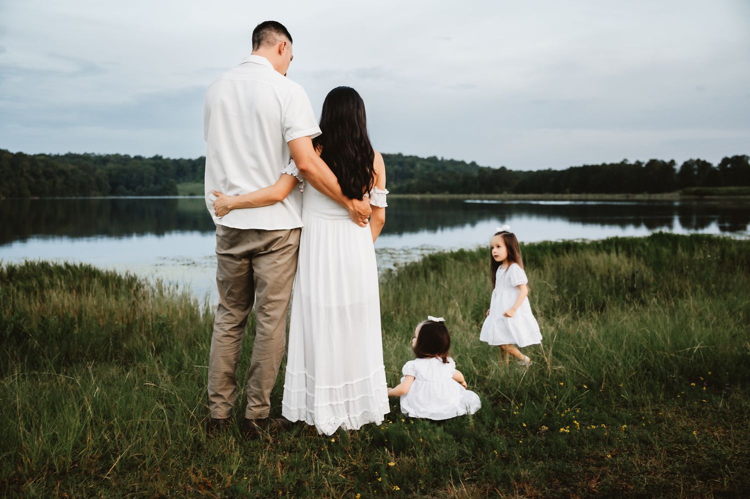 Family wearing white outfits stands together in a scenic grassy meadow during golden hour sunset.
