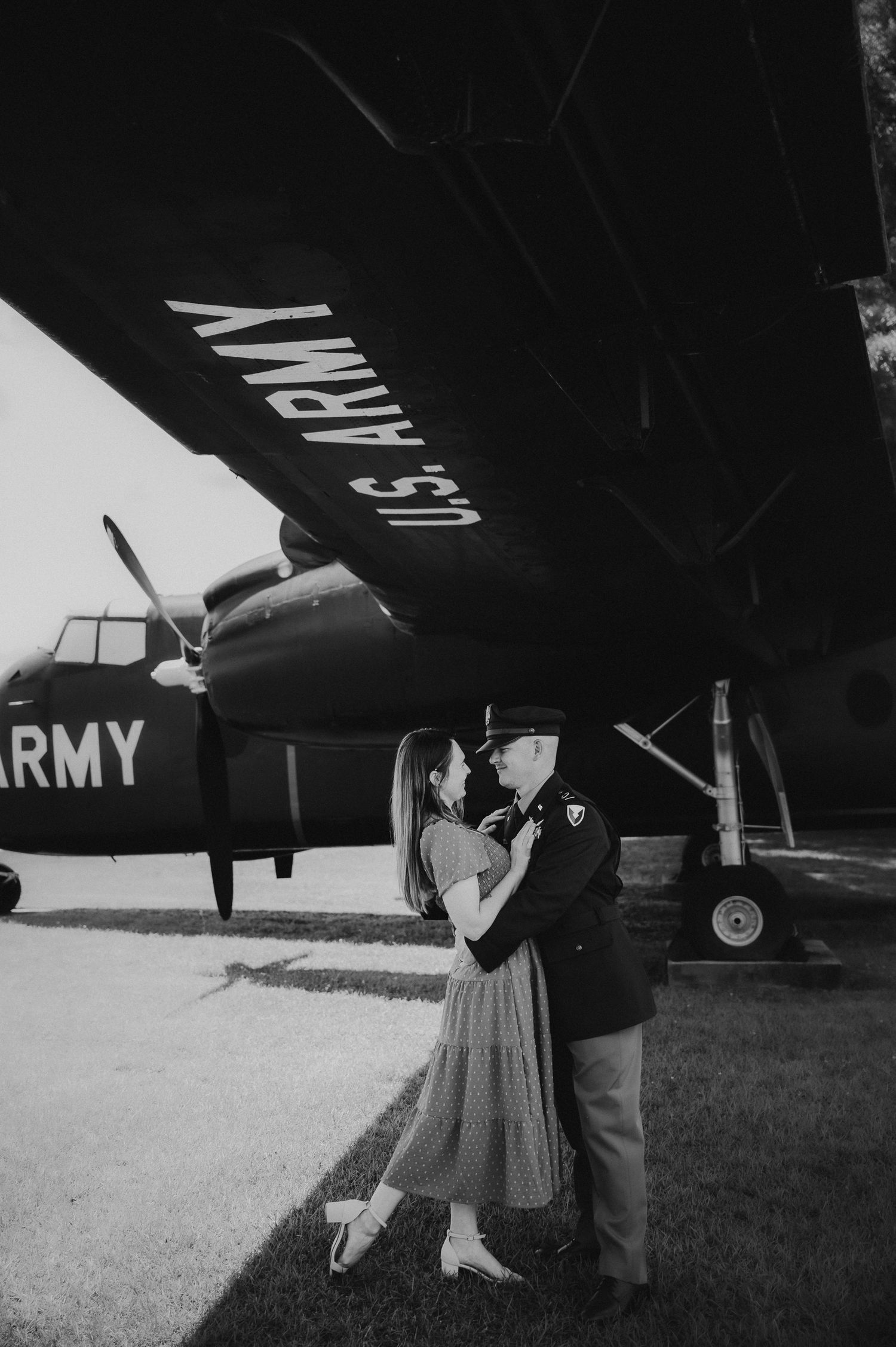 Black and white vintage style photo of couple under U.S. Army aircraft wing.