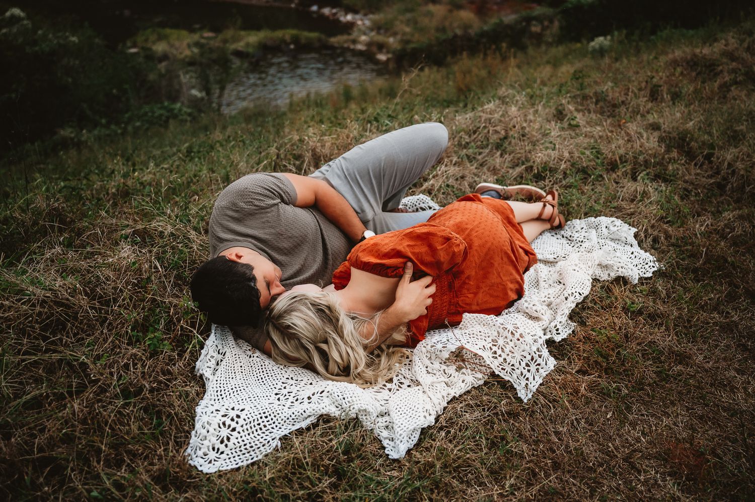 A person lies peacefully on a white lace blanket in the grass during an outdoor photo session.