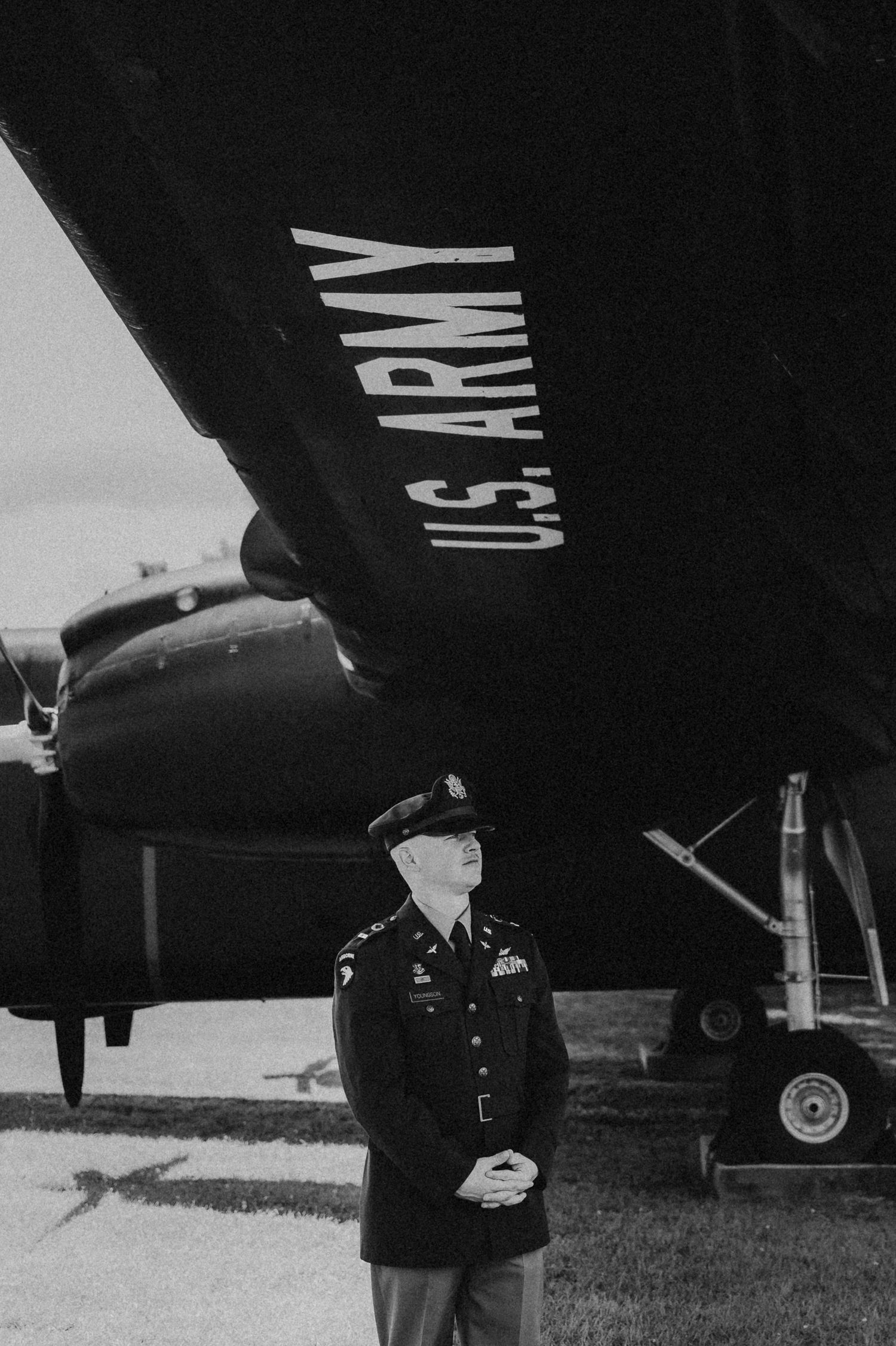 A military service member stands beneath a US Army aircraft in a vintage black and white photograph.