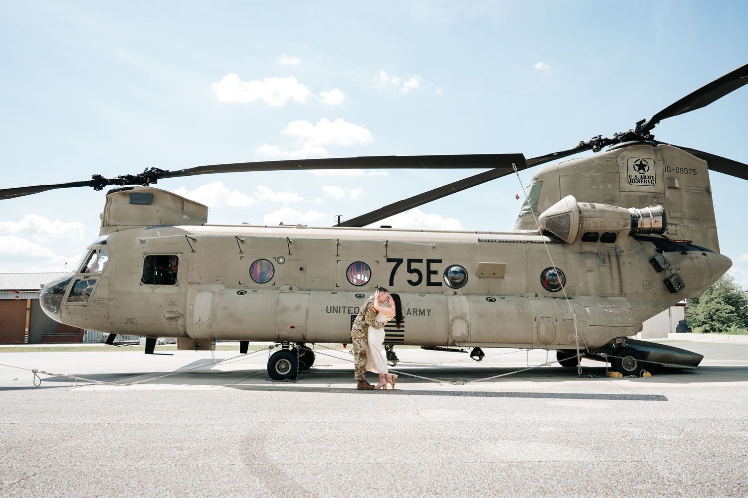Military personnel standing beside a CH-47 Chinook helicopter marked 75E on a tarmac under a partly cloudy sky.