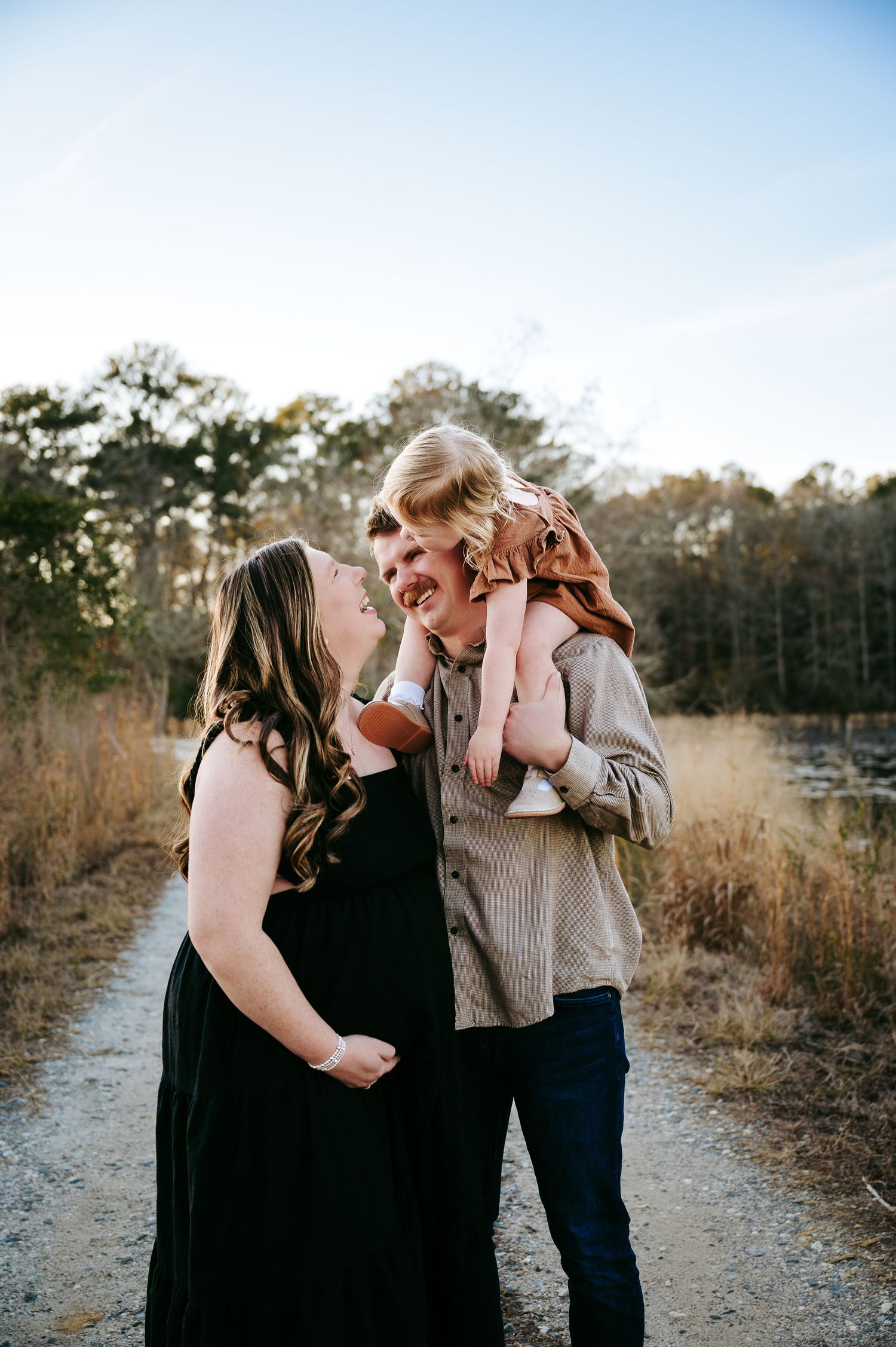A couple shares an intimate moment on a dirt path while holding a young child in the golden evening light.
