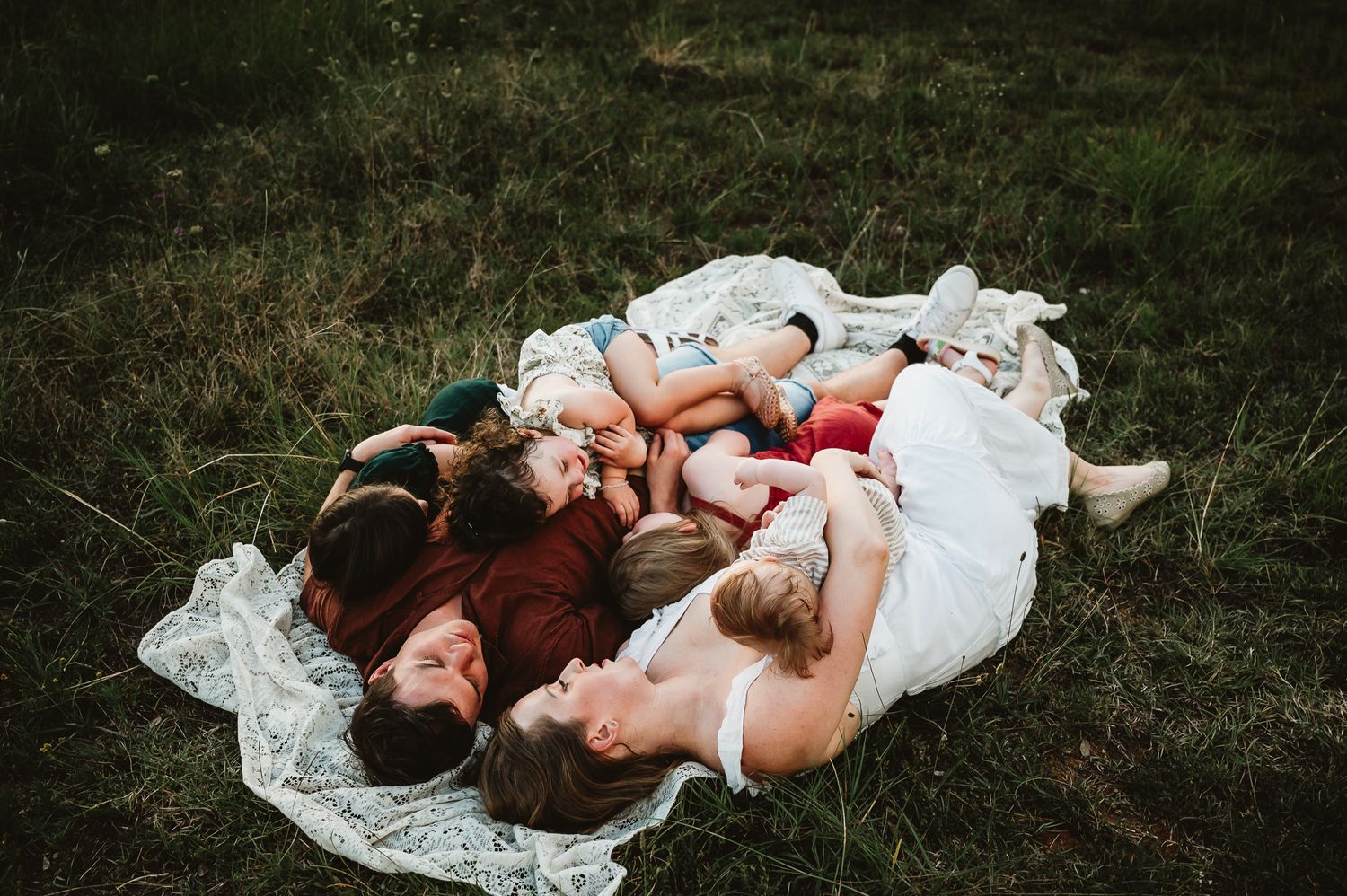 A romantic couple lies together on a blanket in the grass on a sunny day.