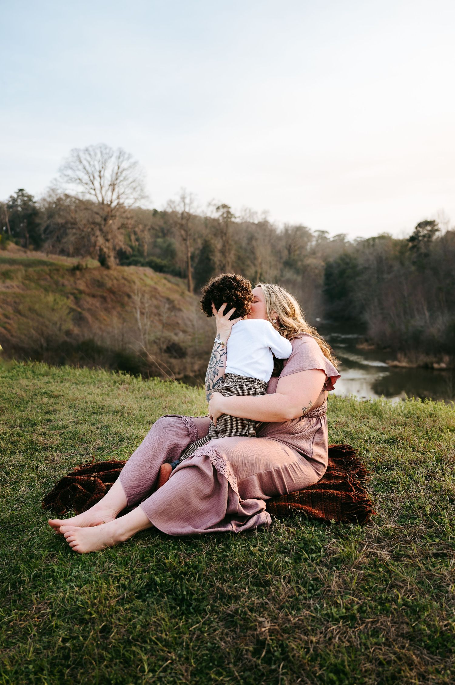 Person in pink dress reclining on grassy hillside during autumn sunset in a dreamy, artistic pose.
