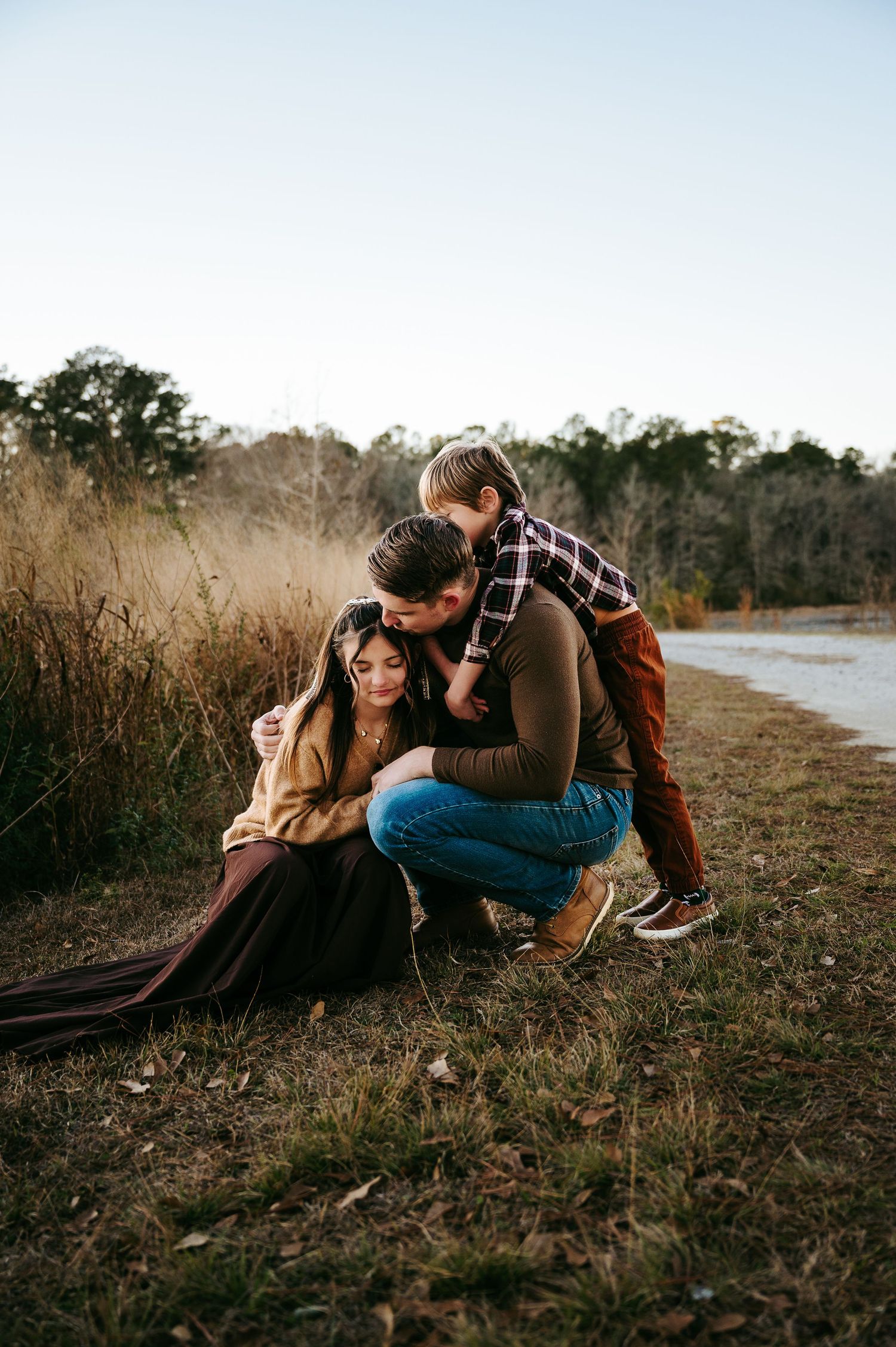 A couple relaxes together in tall grass by a lake during golden hour.