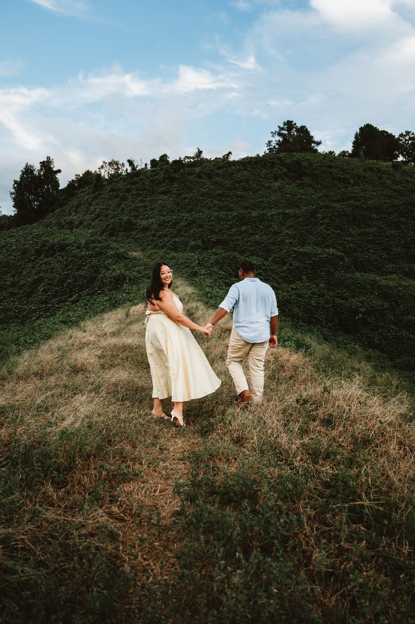 Couple walking hand in hand through a scenic hillside meadow on a bright summer day.