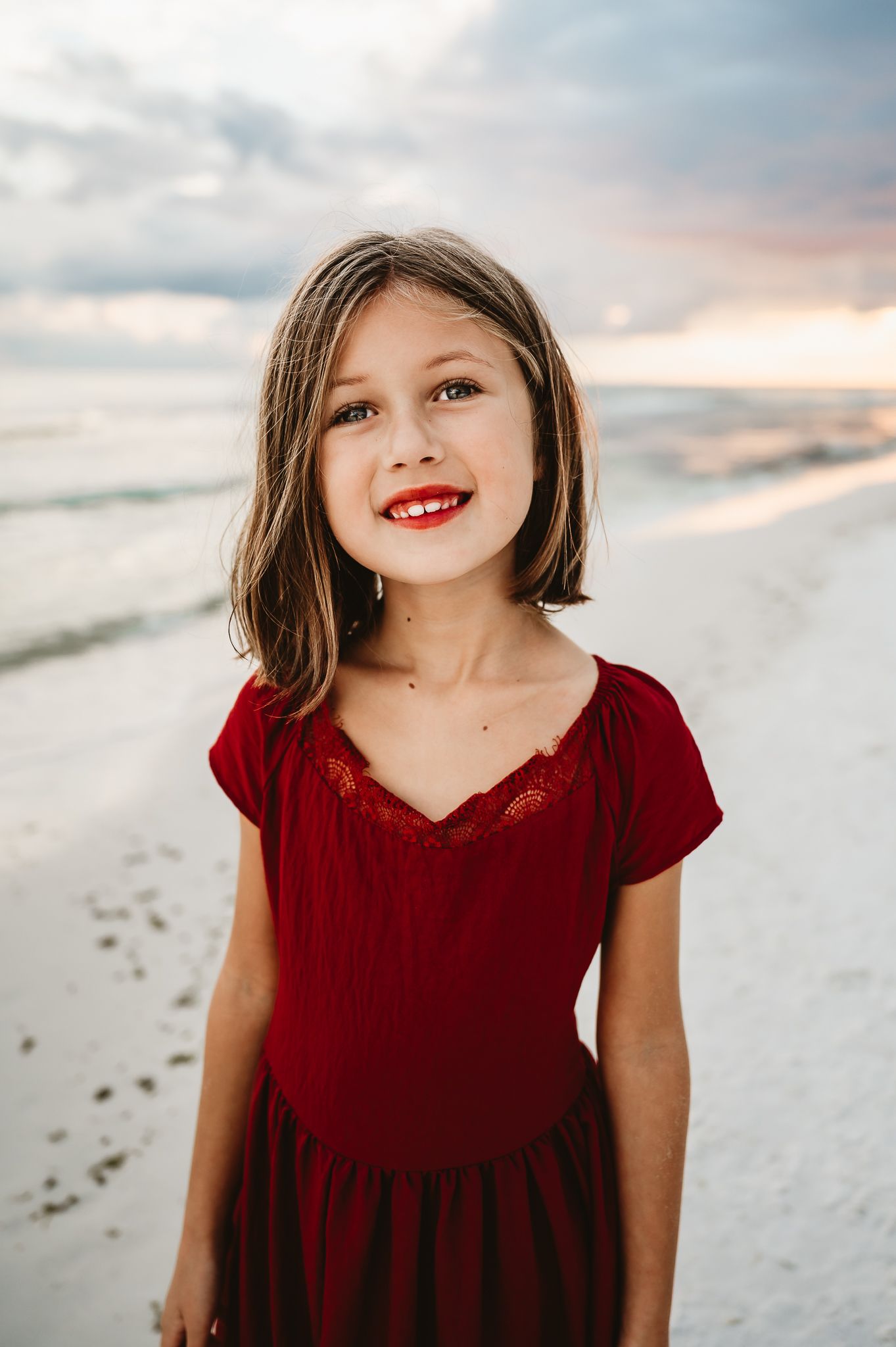 A series of five photos showing someone in a red velvet dress on a white sandy beach at sunset.