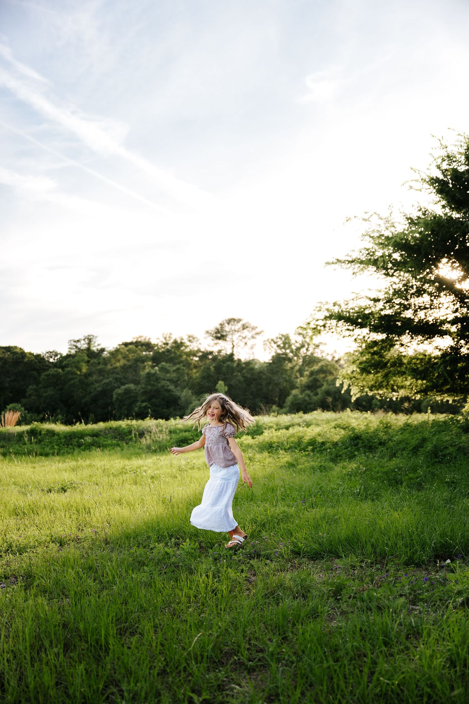 Young girl in white skirt twirling in a lush green meadow during golden hour sunset.