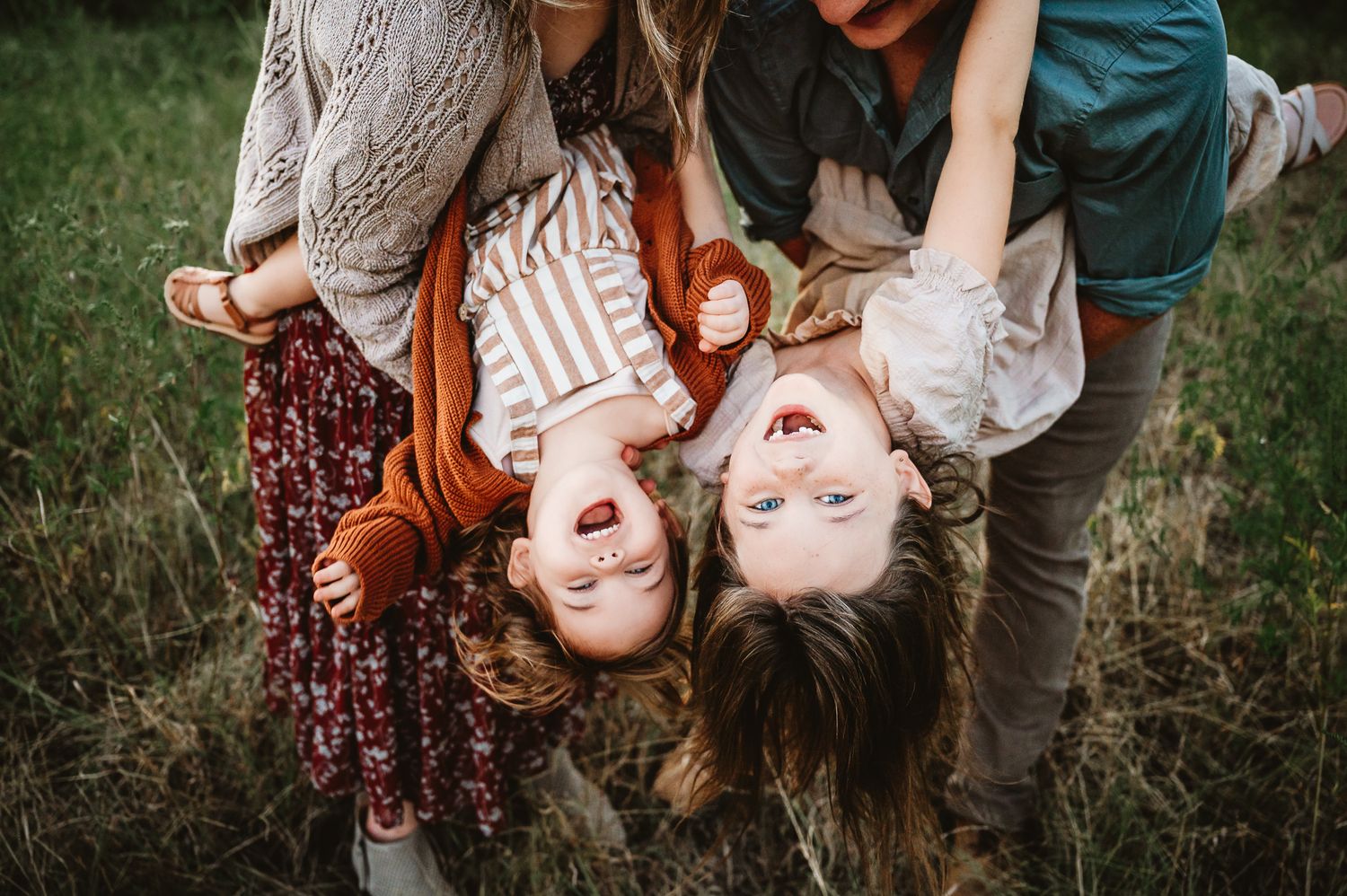 Three people lying in grass together enjoying a playful moment outdoors.