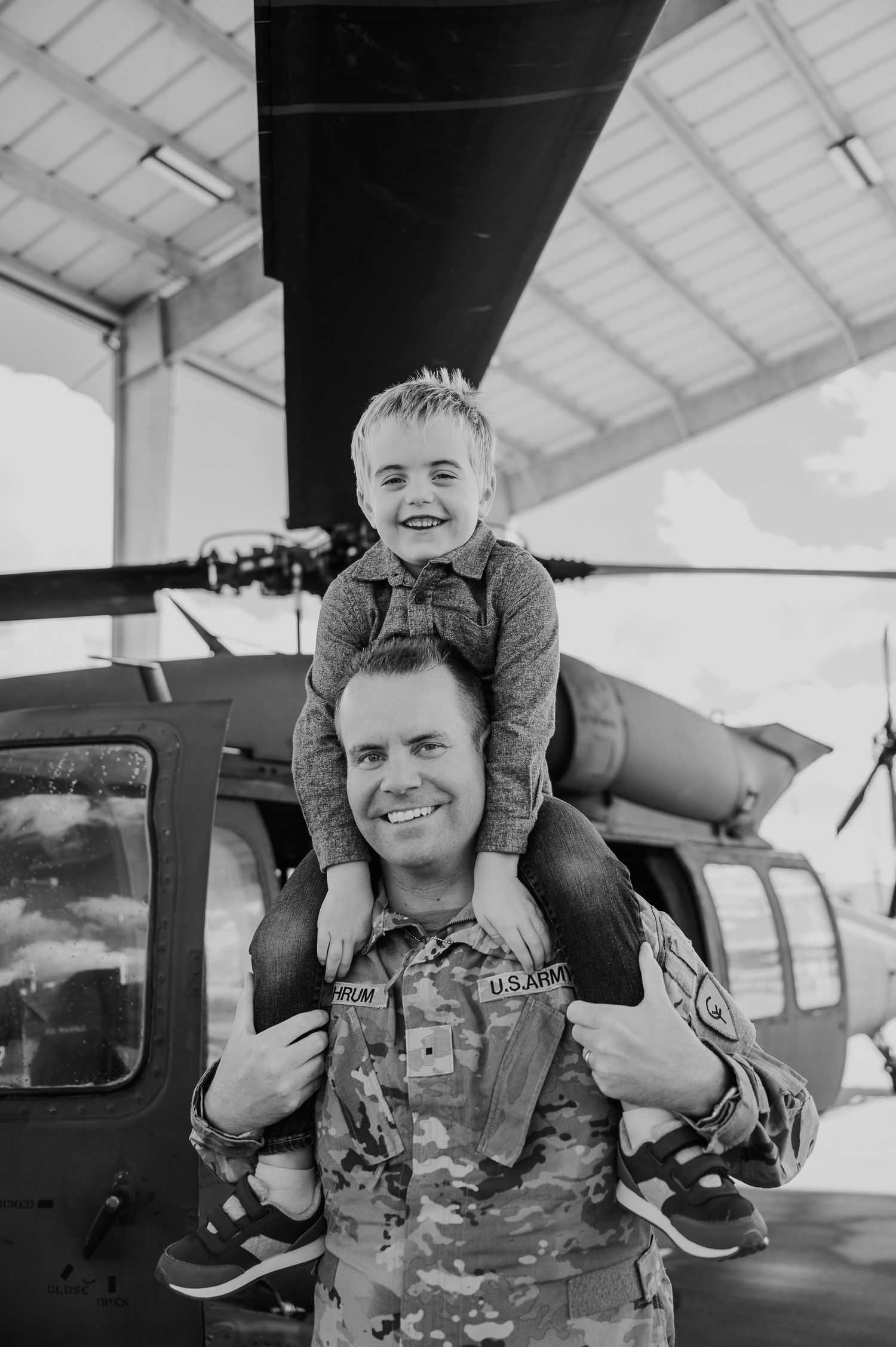 Black and white photo series showing joyful moments between parent and child at an aircraft hangar.
