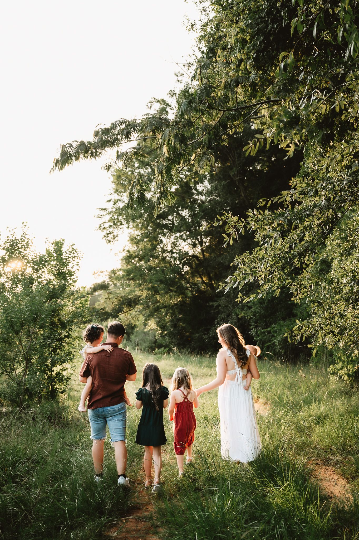 A family walks together on a nature path through lush greenery during golden hour.