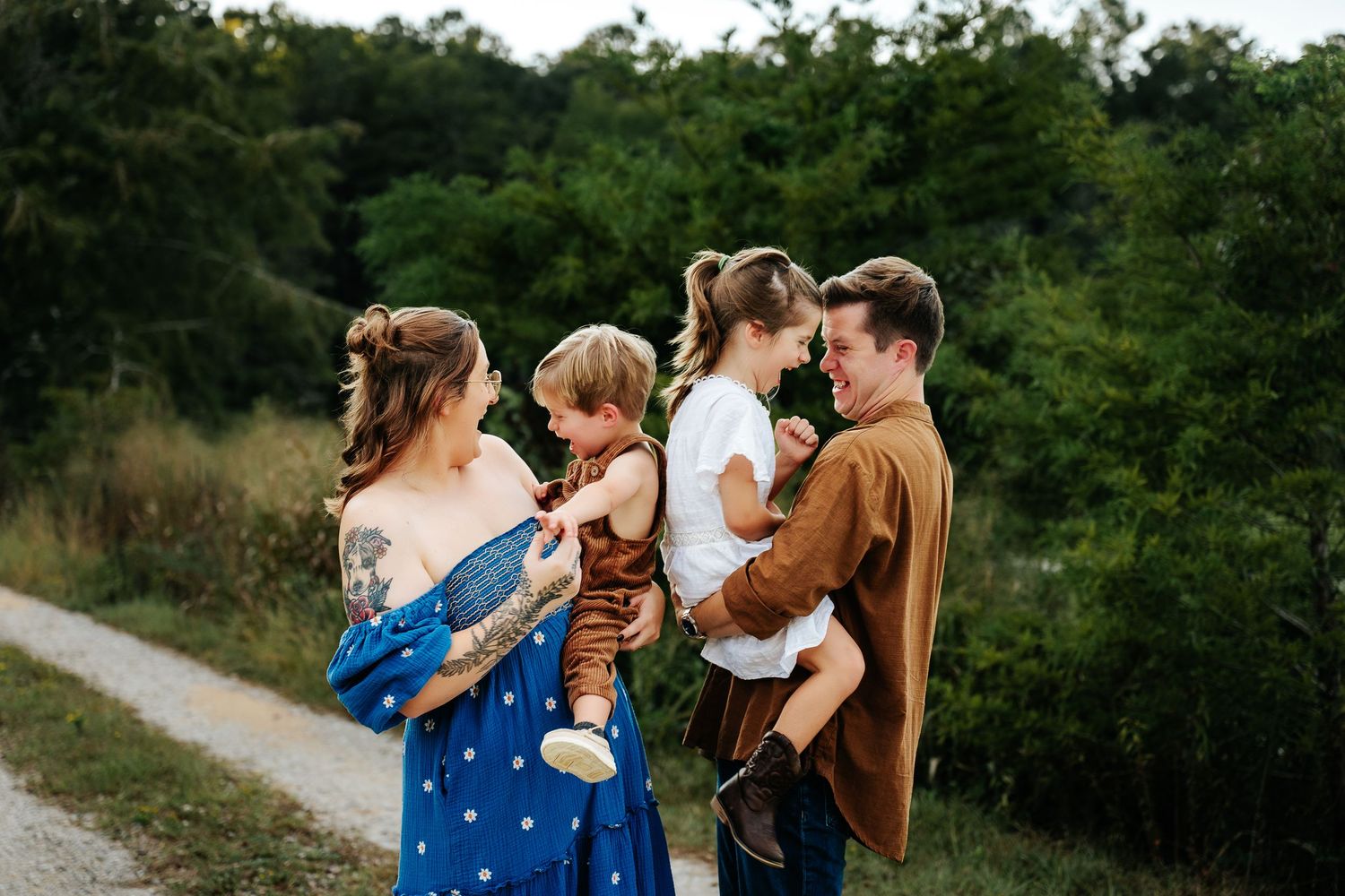 A young family with two toddlers poses on a scenic path surrounded by lush green trees during an outdoor photo session.