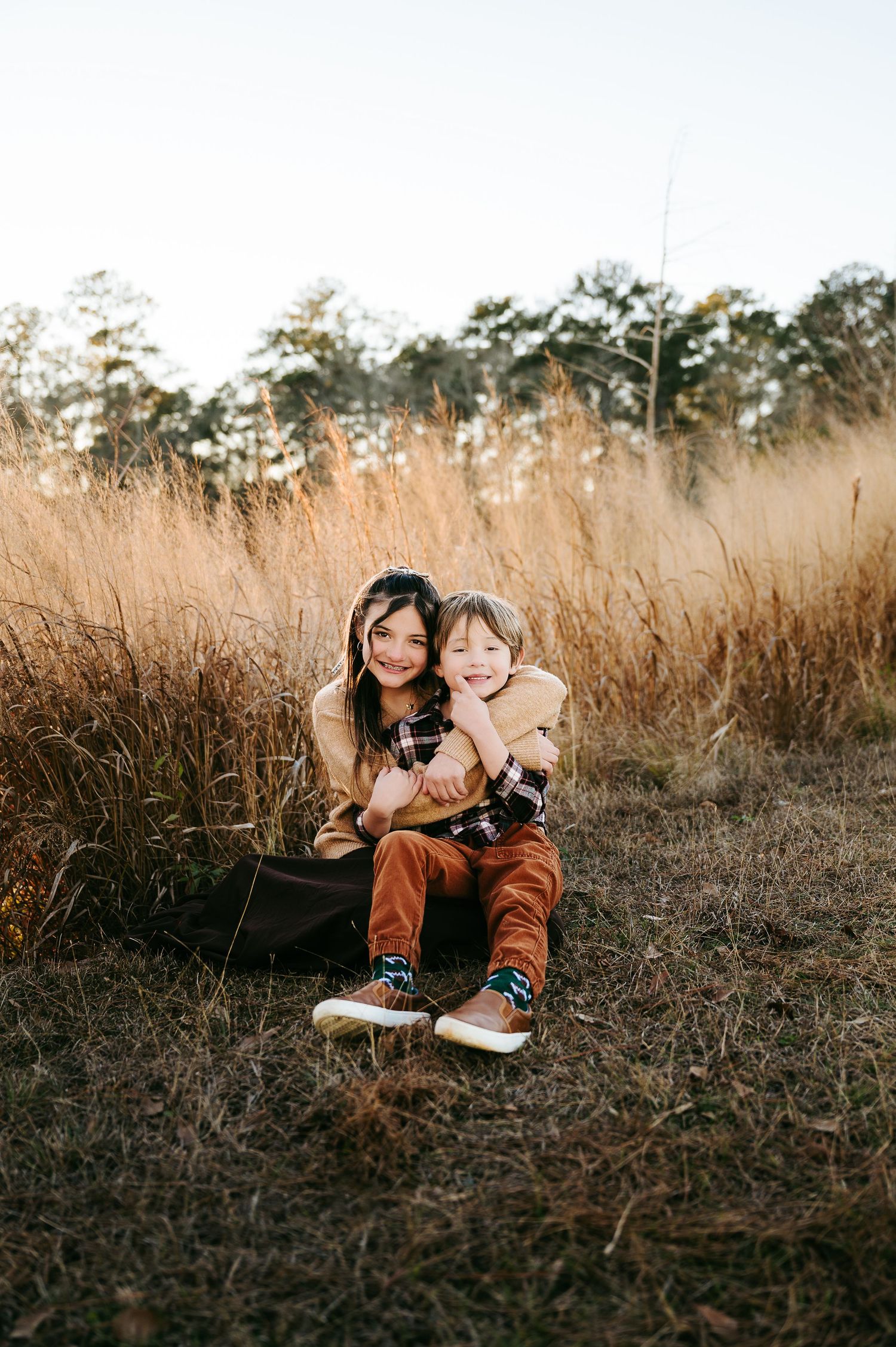 A couple shares an intimate moment while sitting in tall golden grass during sunset.