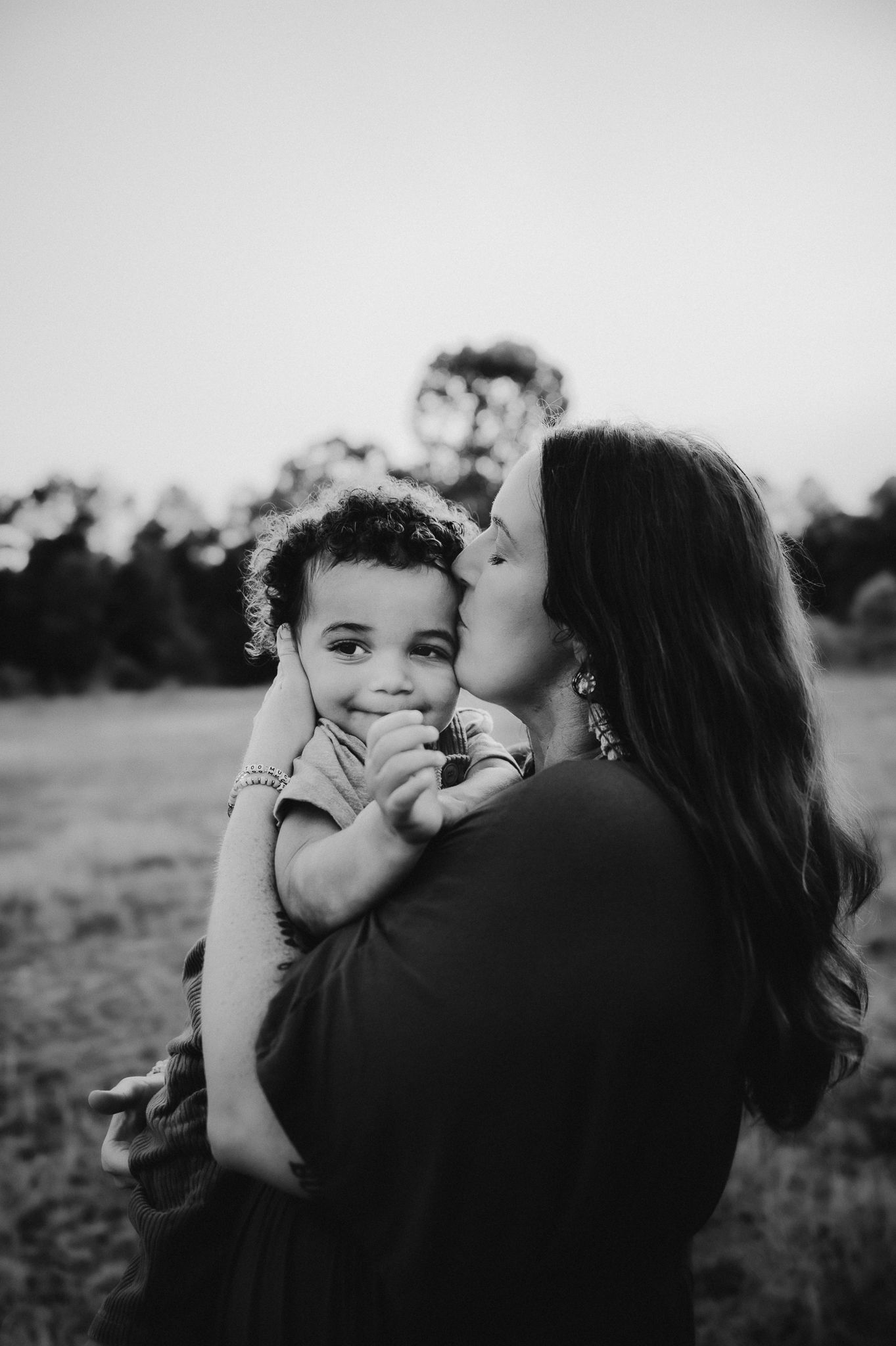 Black and white portrait showing a tender moment between parent and child outdoors at dusk.