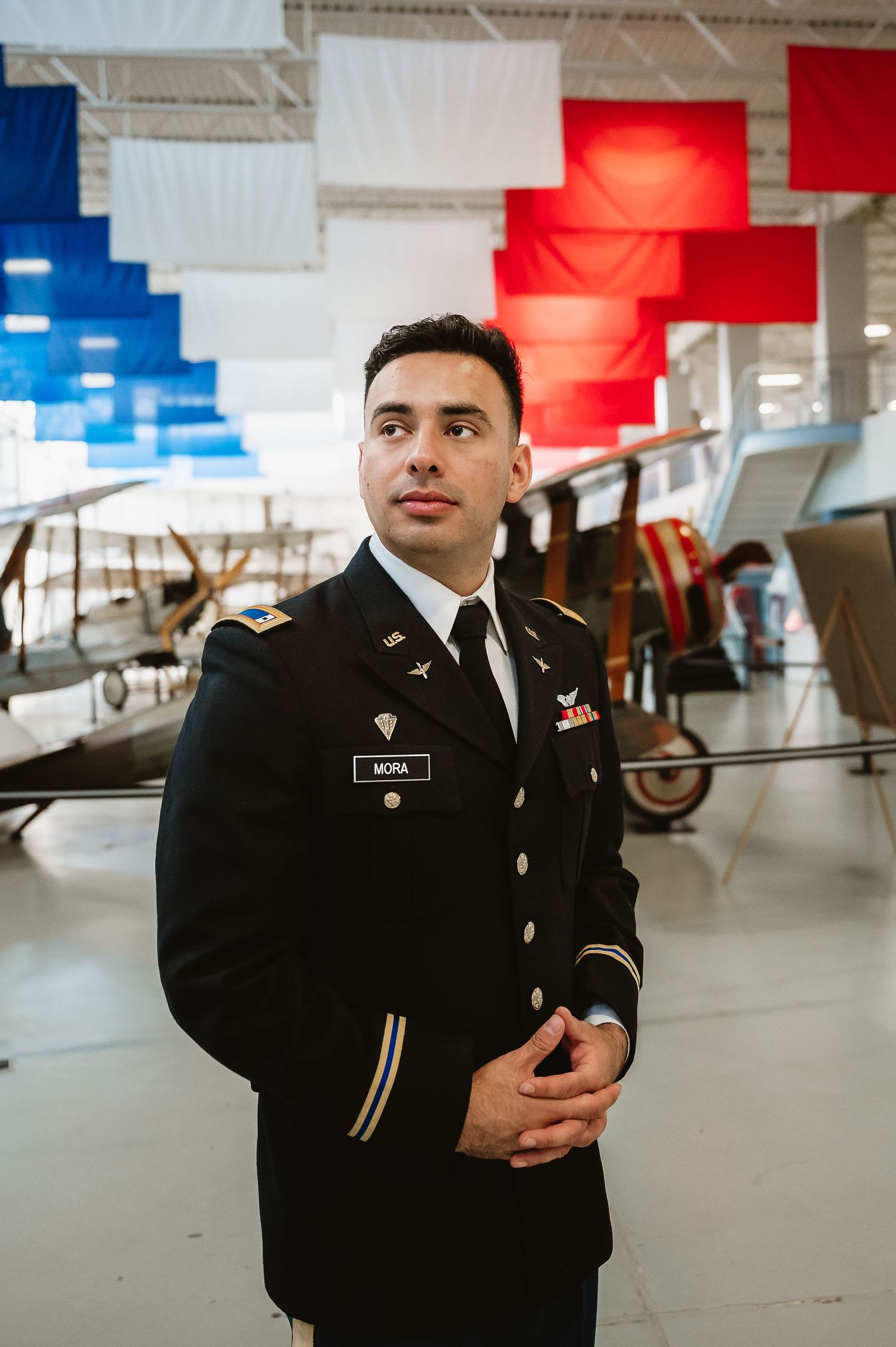 Military service member in dress uniform stands in a parking garage with red and blue lighting.