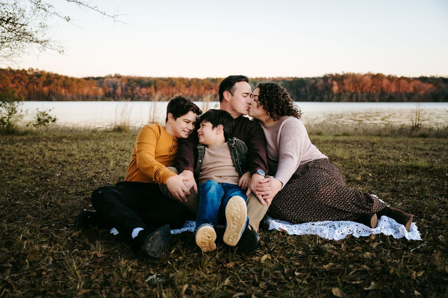 A couple lying on a blanket in a grassy field during autumn sharing an intimate moment at sunset.