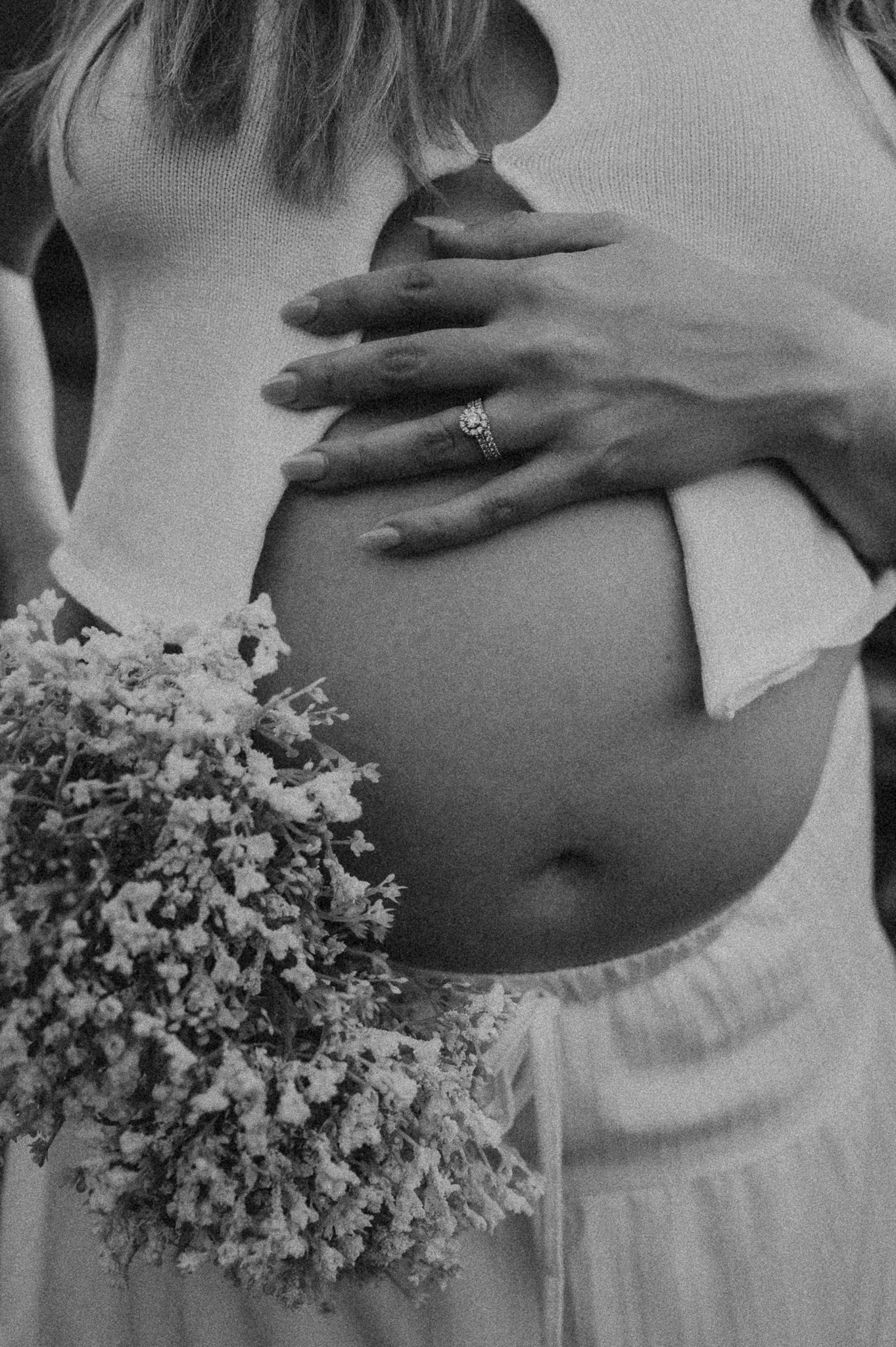 A monochromatic series showing a pregnant belly against flowing white fabric with delicate flower bouquet accents.