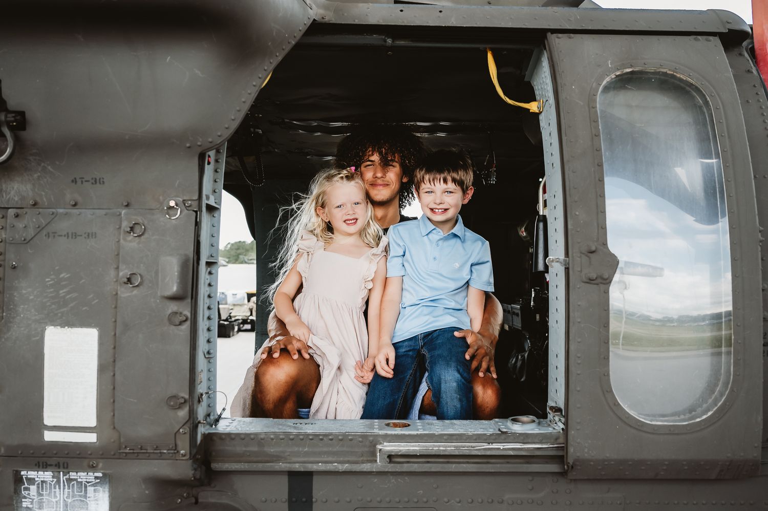 Two children sit in the doorway of a military helicopter on display.