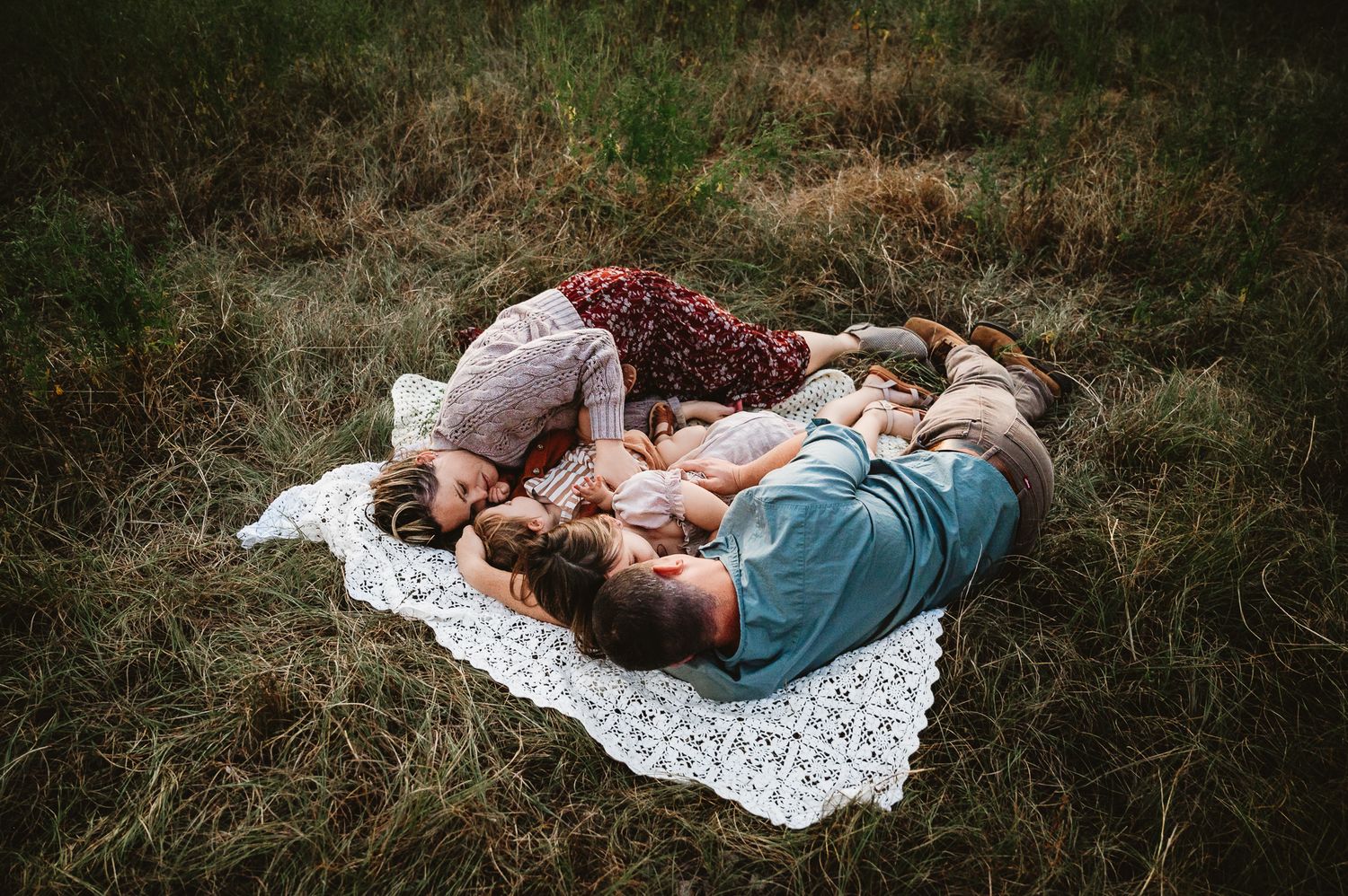 Couple relaxing together on a white lace blanket in a rustic outdoor field during sunset.
