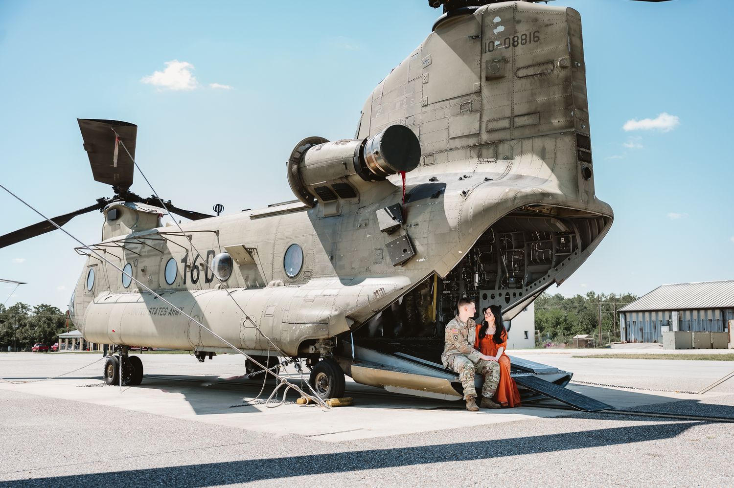 Military CH-47 Chinook helicopter parked on tarmac with cargo doors open and against blue sky background.