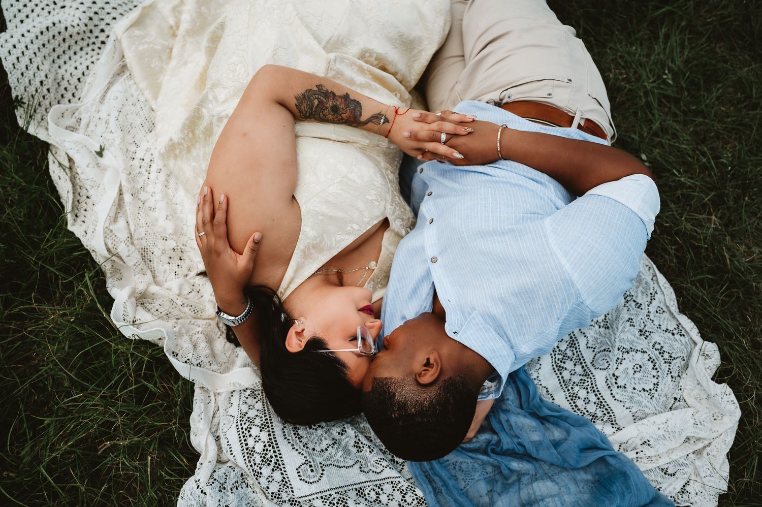 A couple in white lace and denim lying together in romantic poses on dark grass.