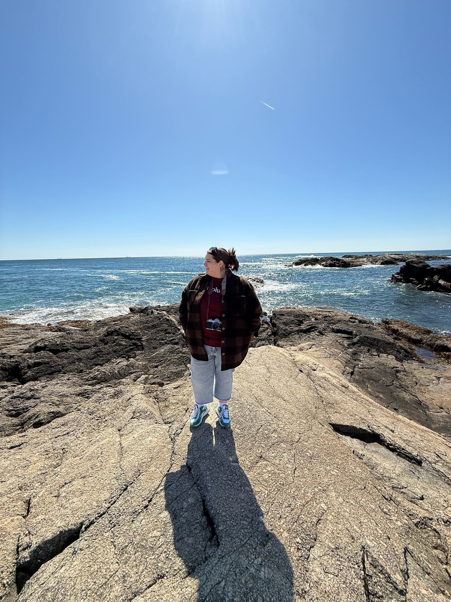 Rocky coastal landscape with crashing waves and rugged stone formations under bright blue sky.