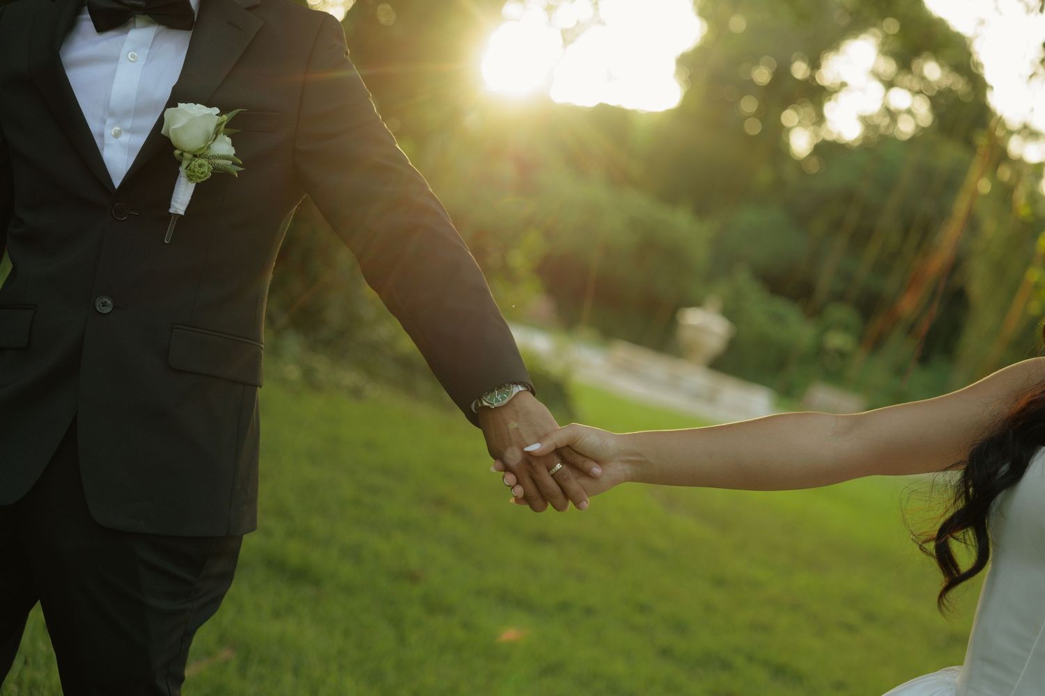 Bride and groom holding hands at golden hour in a lush garden, showcasing wedding attire and romantic sunset lighting.
