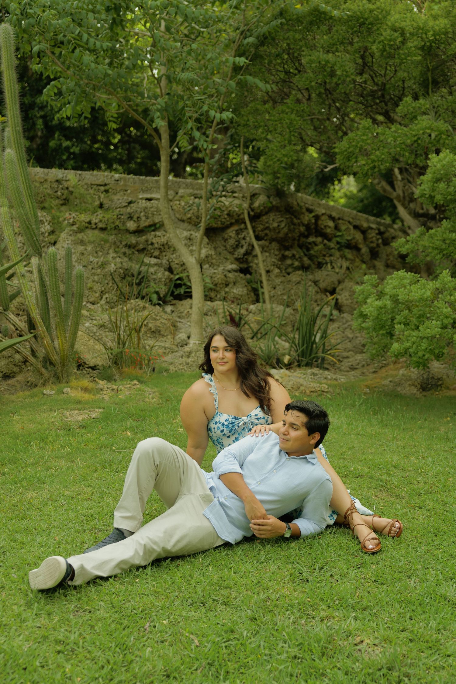 Couple relaxing on green grass in a lush garden, woman sitting up while man reclines against her outdoors.
