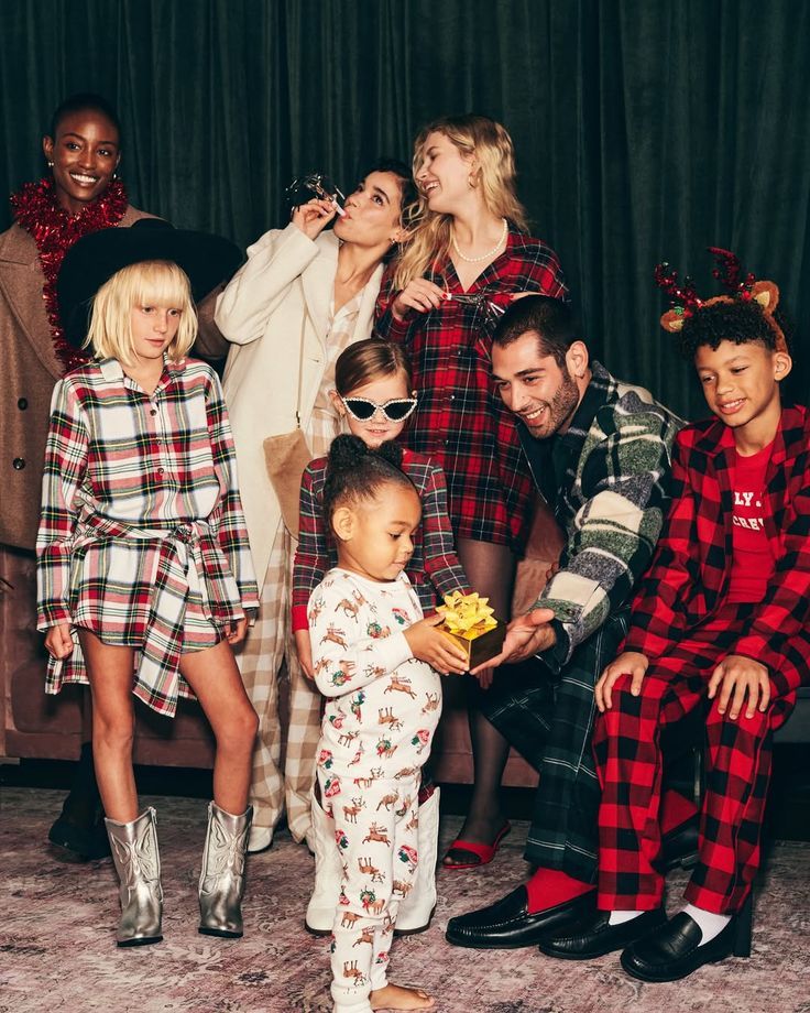 Family group in festive plaid and holiday pajamas posing together for a Christmas photo with gifts and reindeer antlers.
