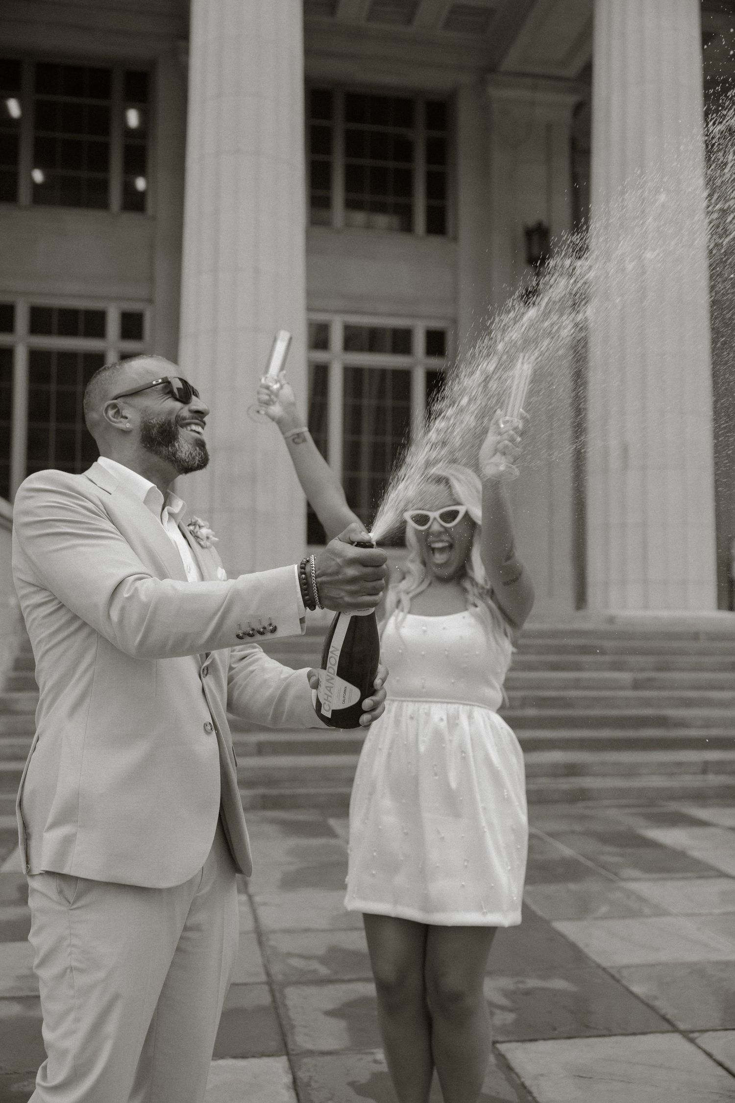 A sequence of four black and white photos showing a couple celebrating with champagne on stone steps.