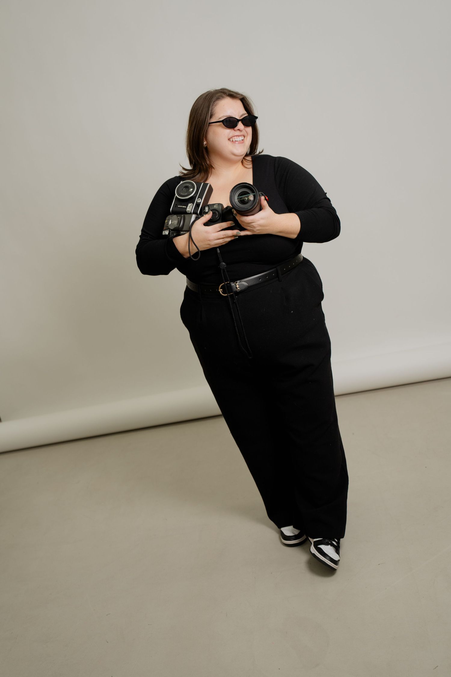 A person wearing black clothing sits and poses in various positions against a light gray studio backdrop.