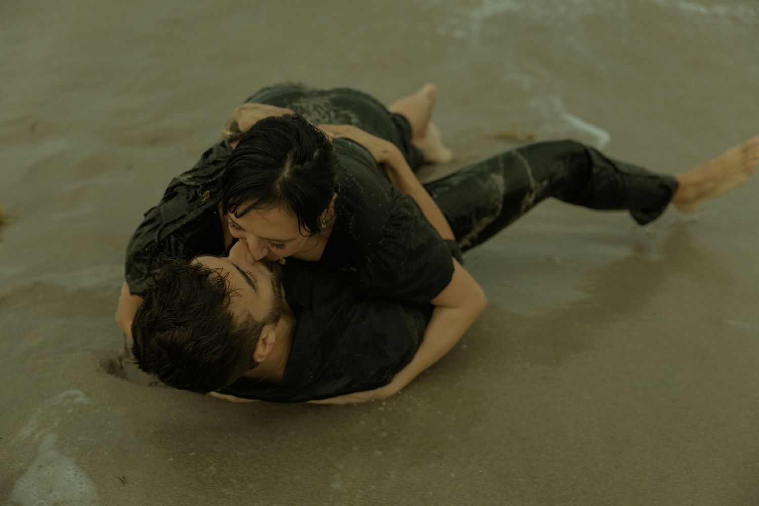 A figure in a black dress performs a graceful dance movement in shallow water at sunset.