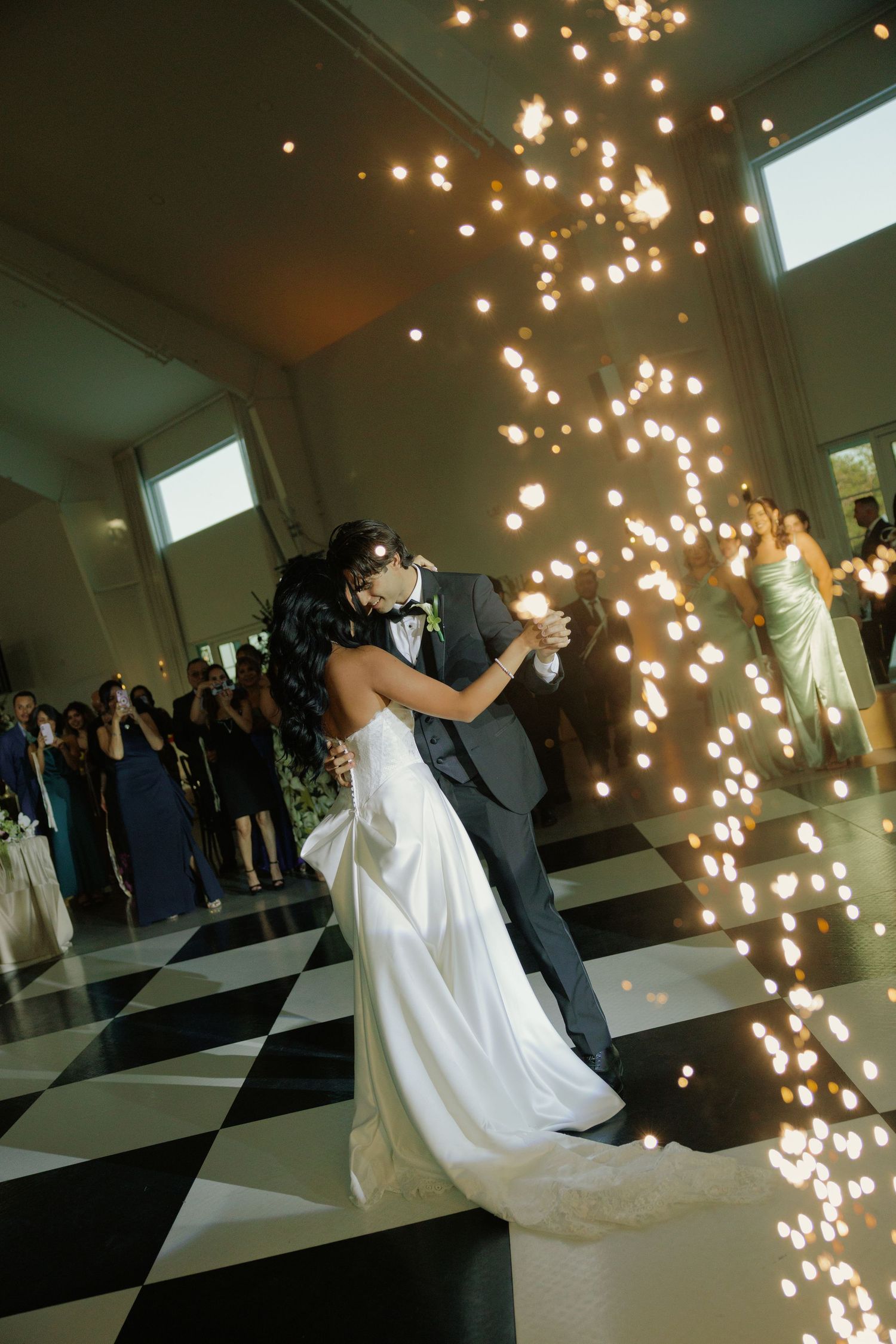 Bride and groom share first dance on checkered floor surrounded by sparkling cold pyrotechnics at elegant wedding reception.