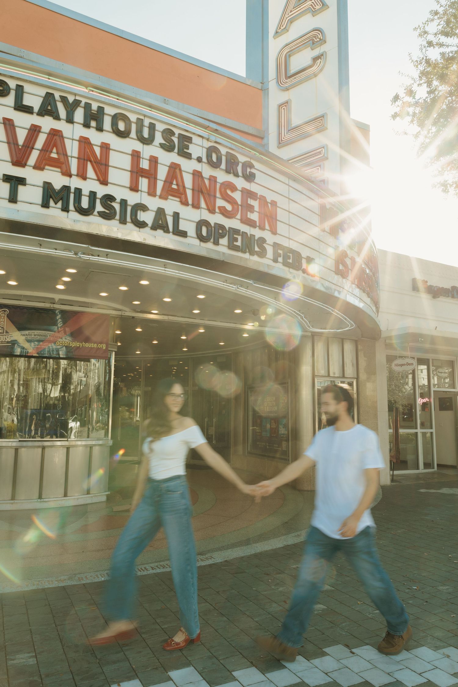 Two people hold hands and dance in front of a vintage theater marquee displaying 