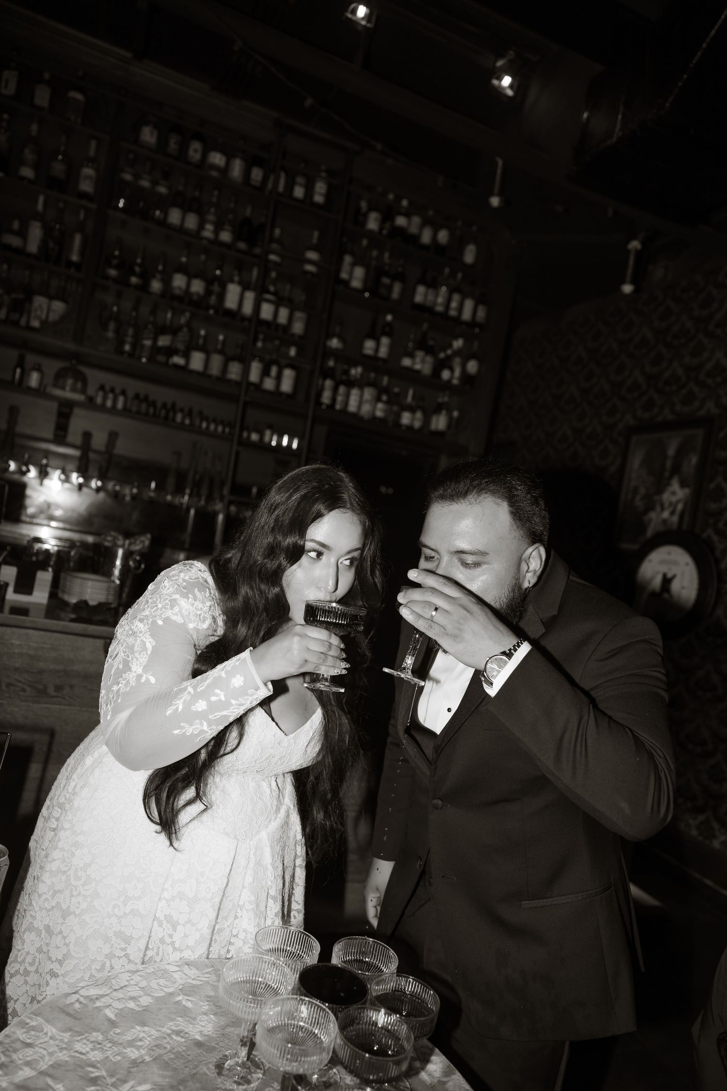 Bride and groom sharing a drink together at a dark romantic bar in black and white photo.