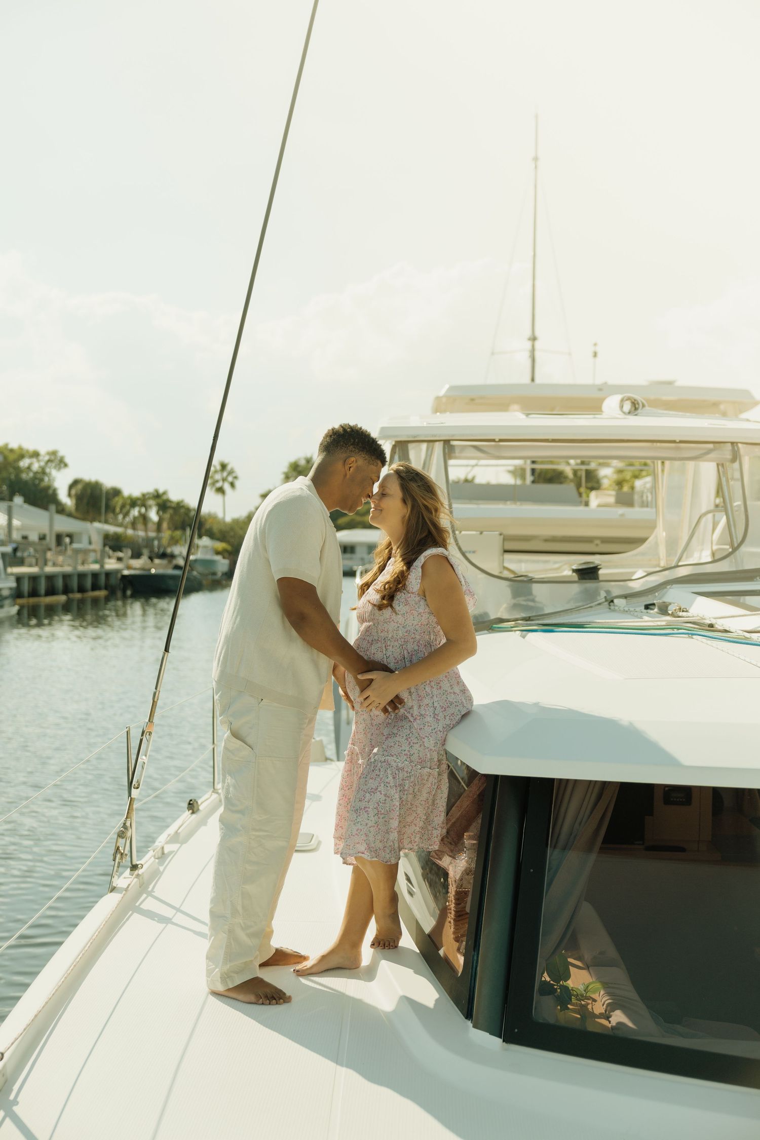 A romantic couple shares intimate moments aboard a yacht on a sunny day by the water.